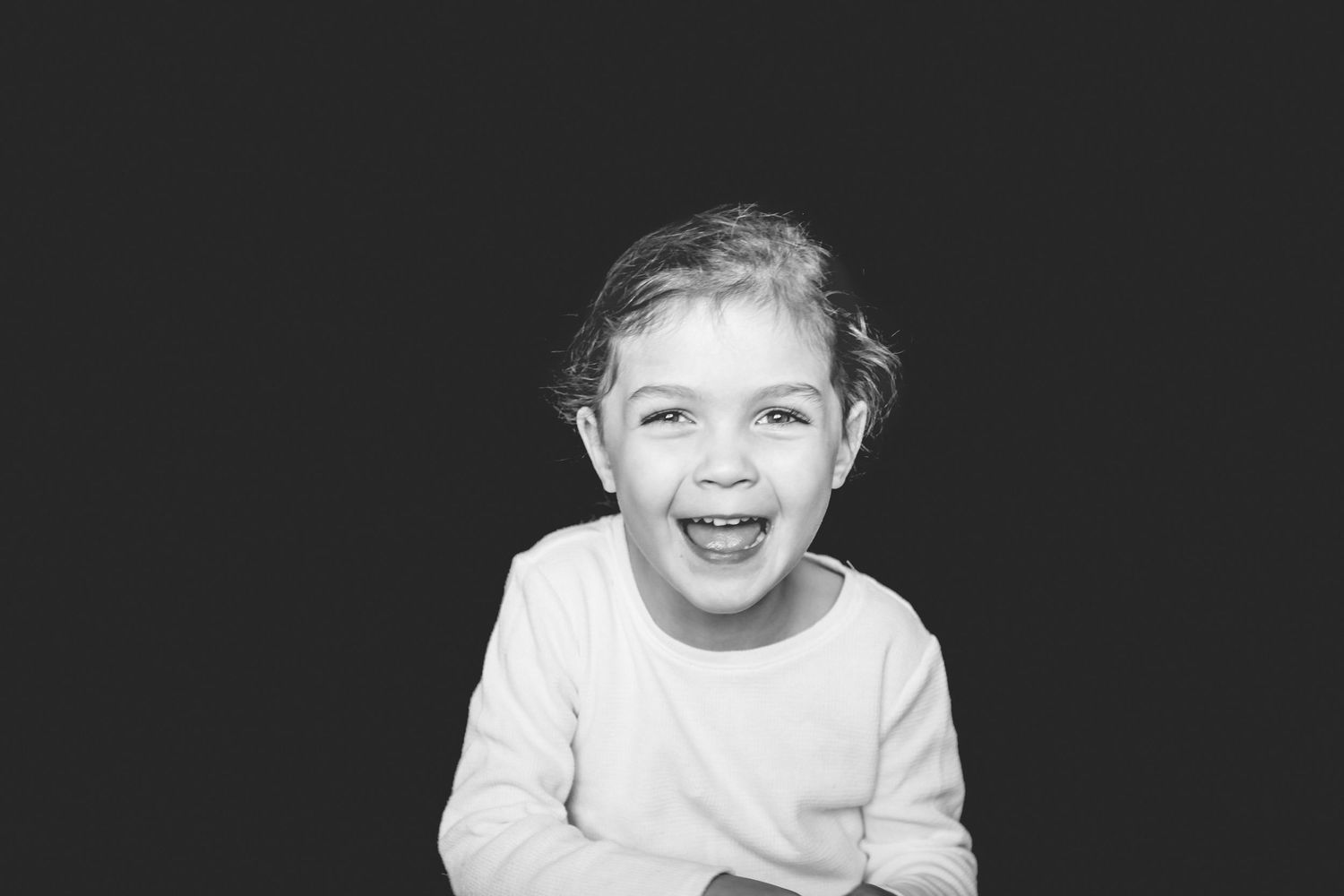 Black and white portrait of a young child laughing joyfully against a dark background.
