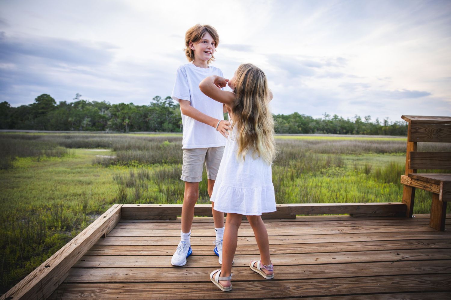 Two people in white outfits dancing together on wooden deck with marsh landscape behind them.