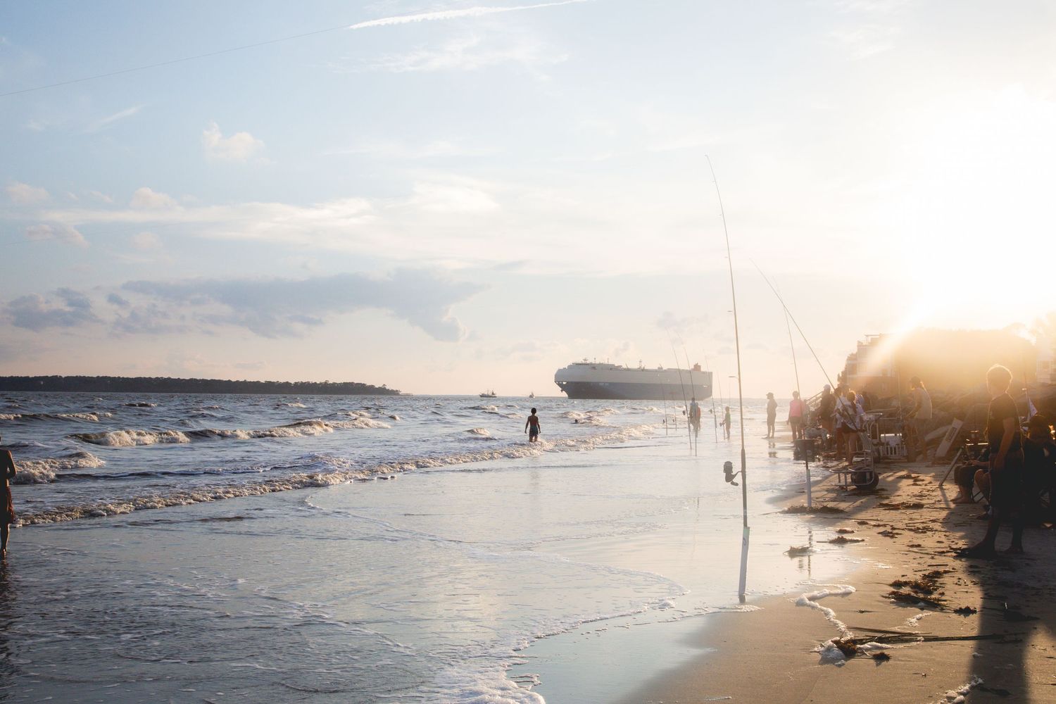 A serene beach landscape with fishing poles set up along the shoreline at golden hour.