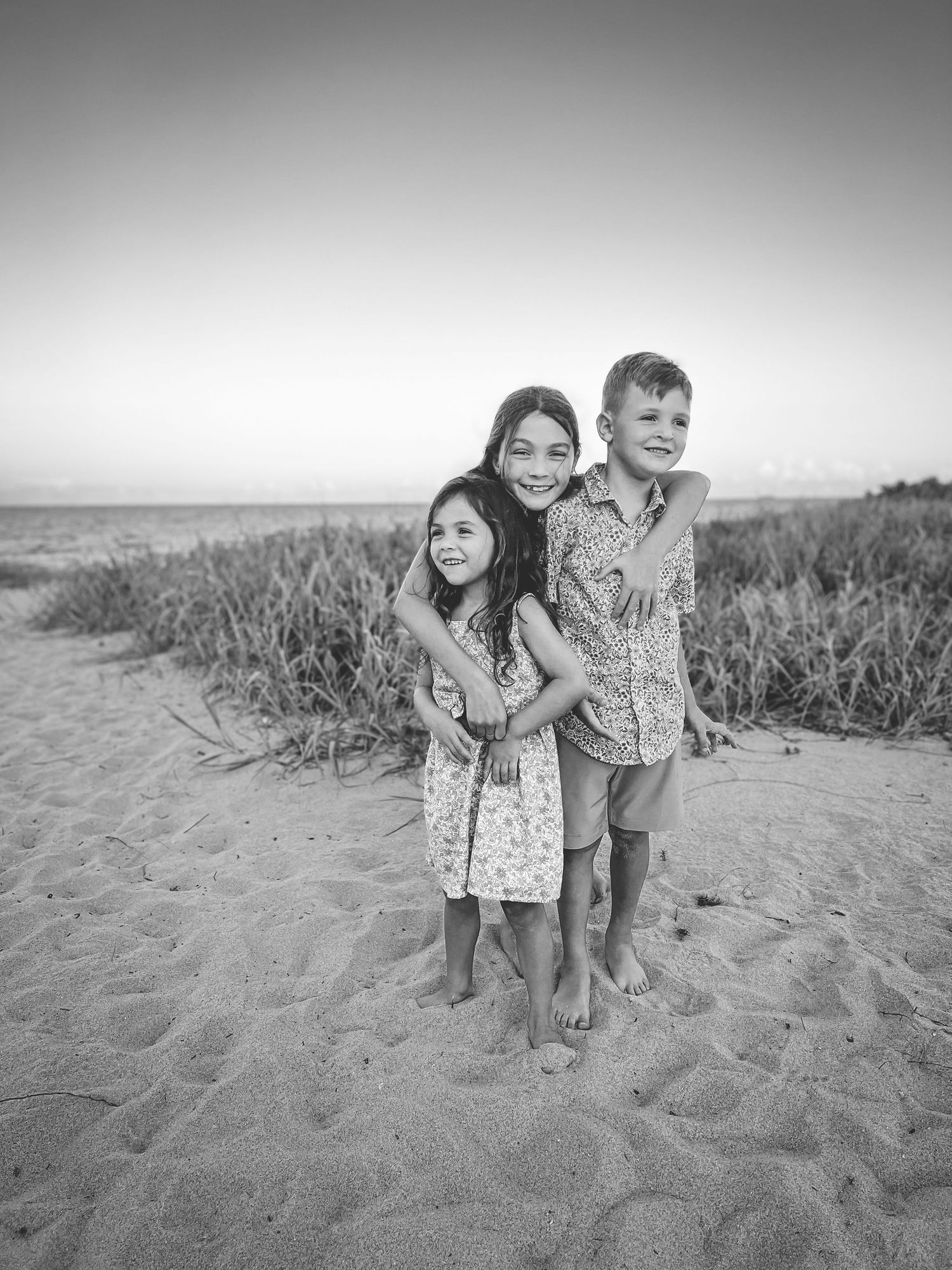 Young children playing together on a sandy beach in black and white.