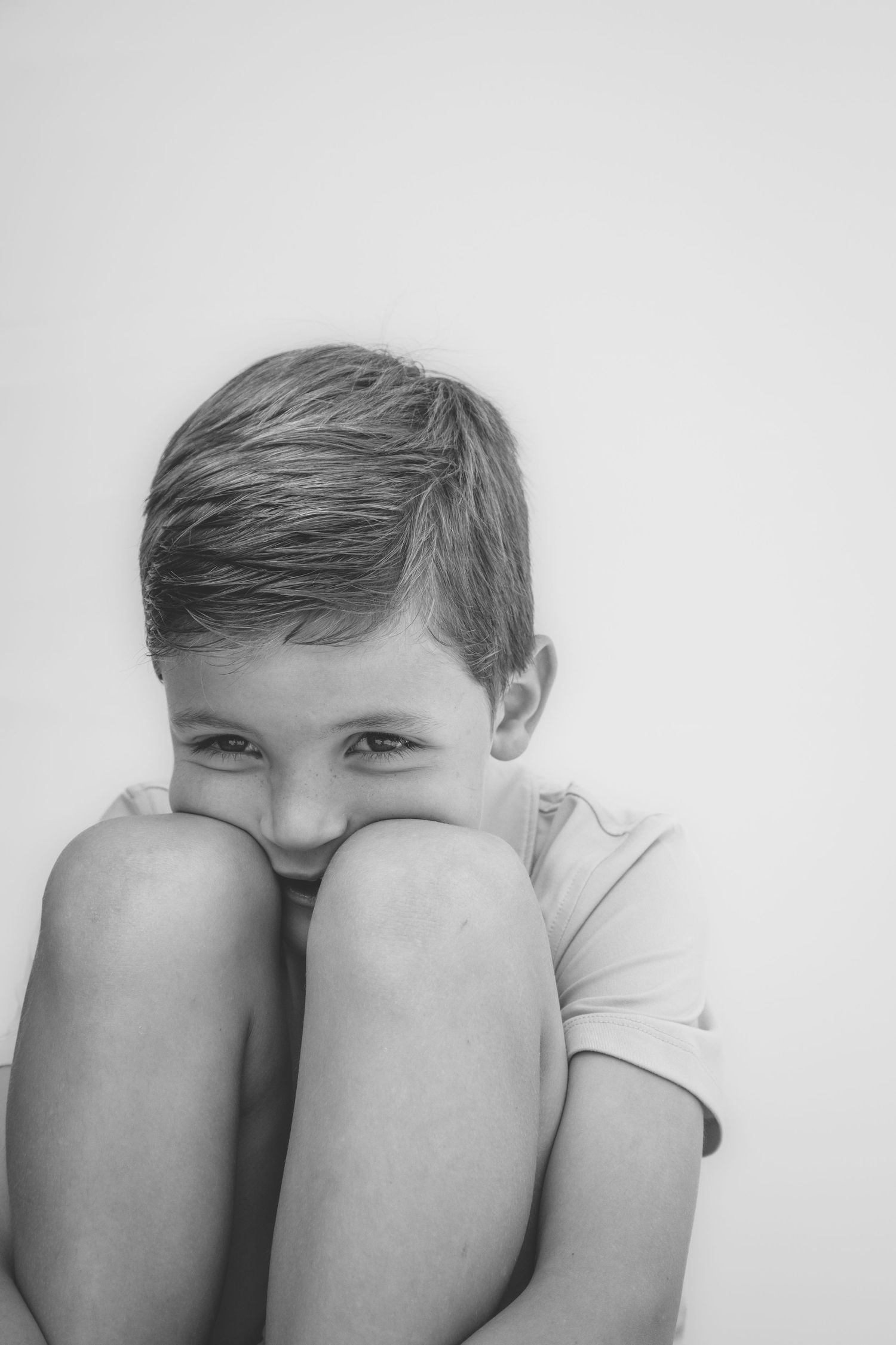 A black and white portrait of a child hugging their knees close to their chest in a playful pose.