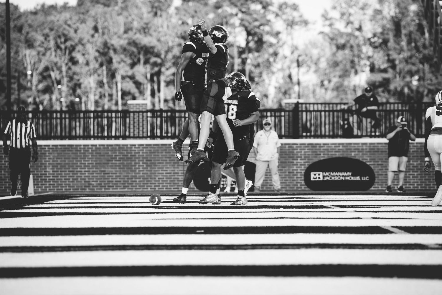 Players celebrate a touchdown on the football field in black and white photography.