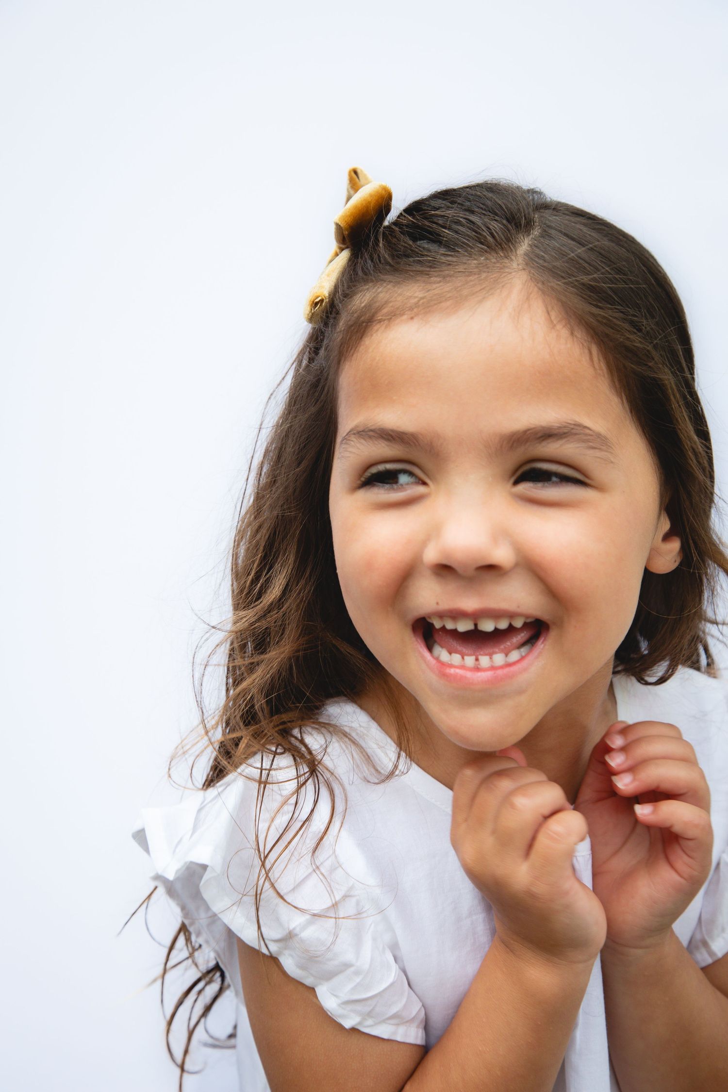 A joyful young child in a white dress laughs with excitement against a light background.