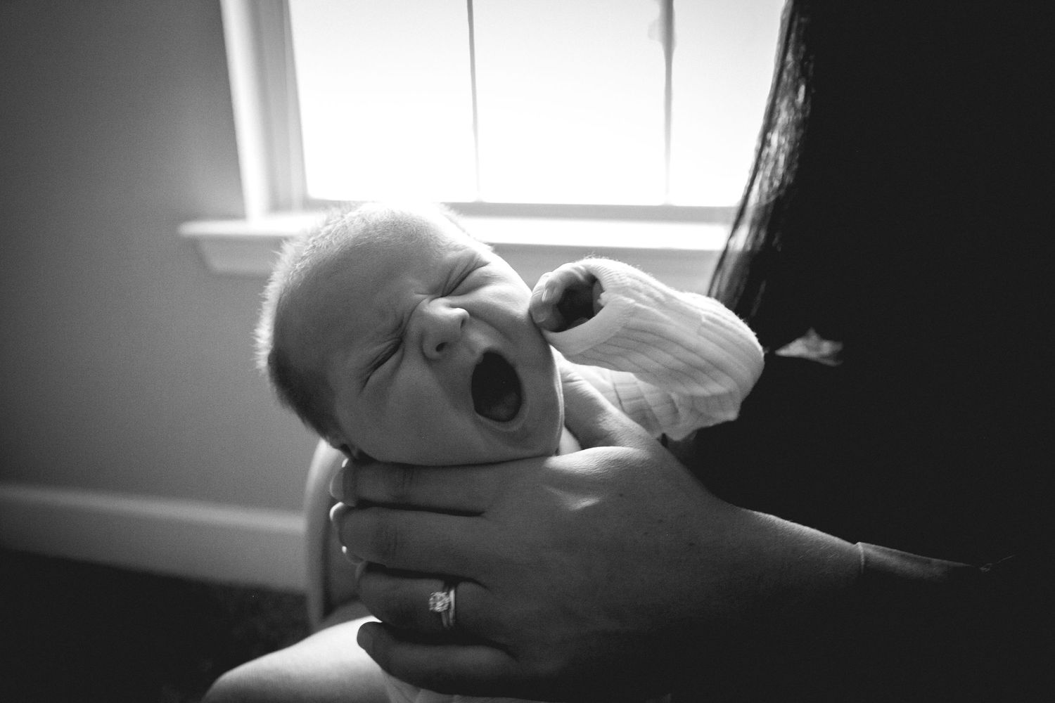 A black and white photo of a yawning baby being cradled in someone's hands.