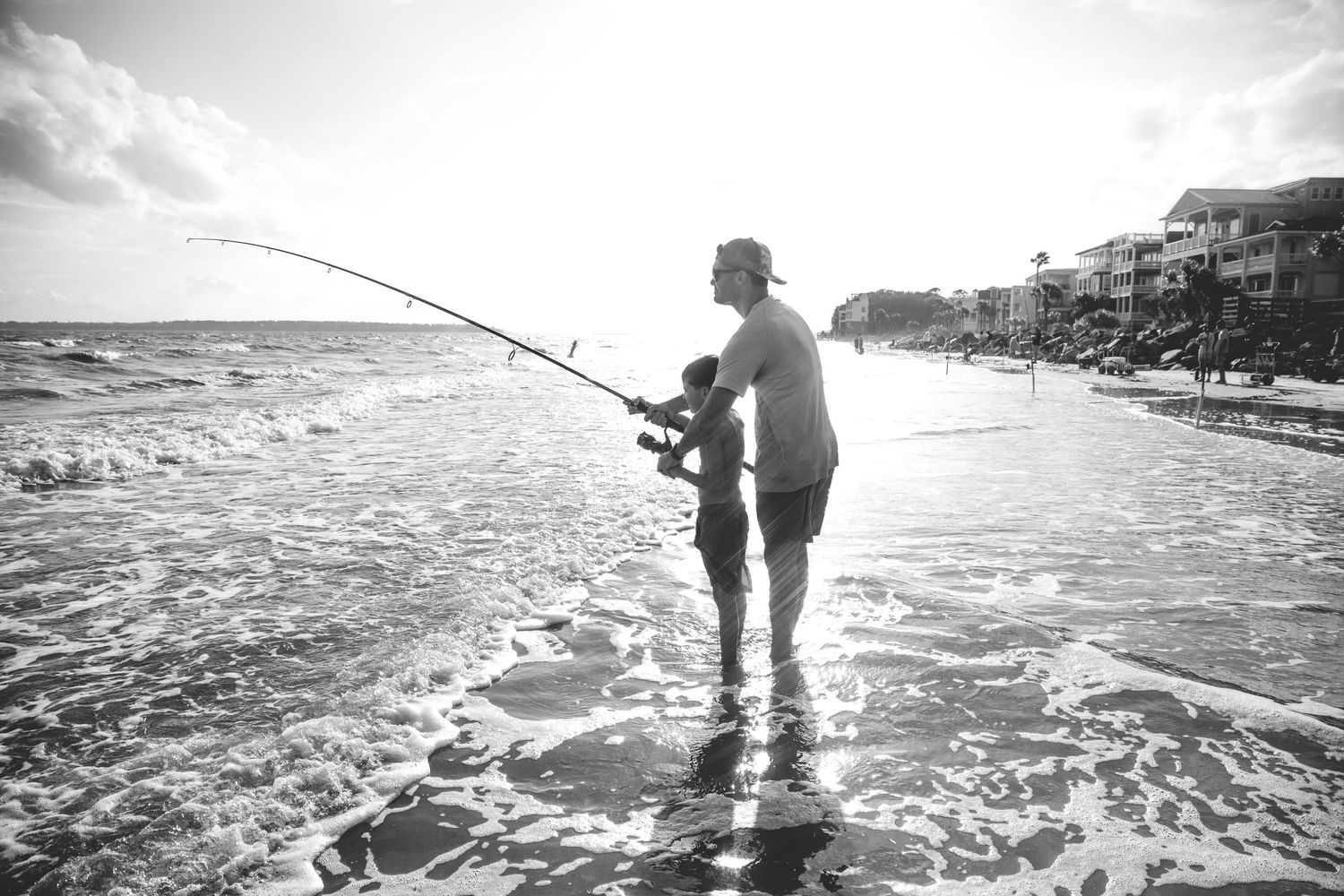 Group fishing from the beach with fishing rods extended over calm ocean waters.