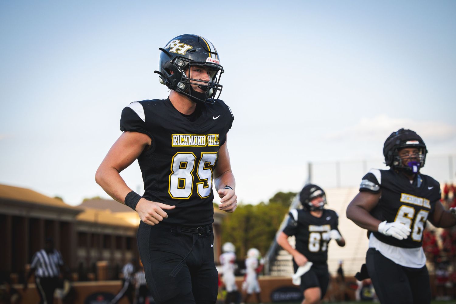 High school football players in black uniforms celebrate on field during evening game under lights.