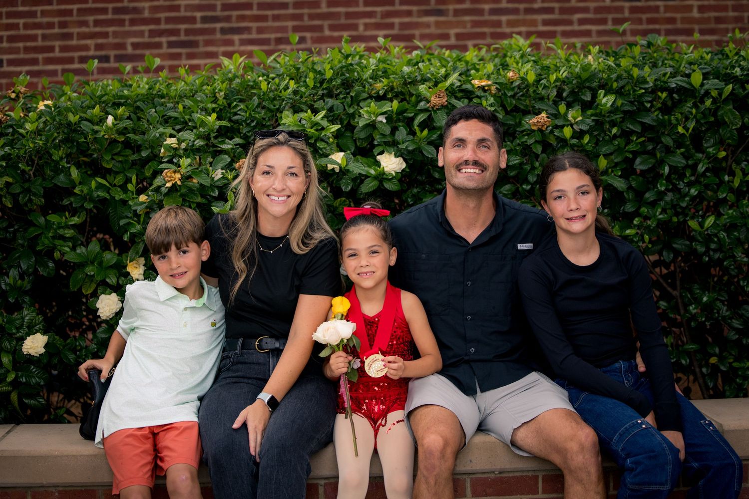 Extended family sitting together for an outdoor portrait session against a brick wall.
