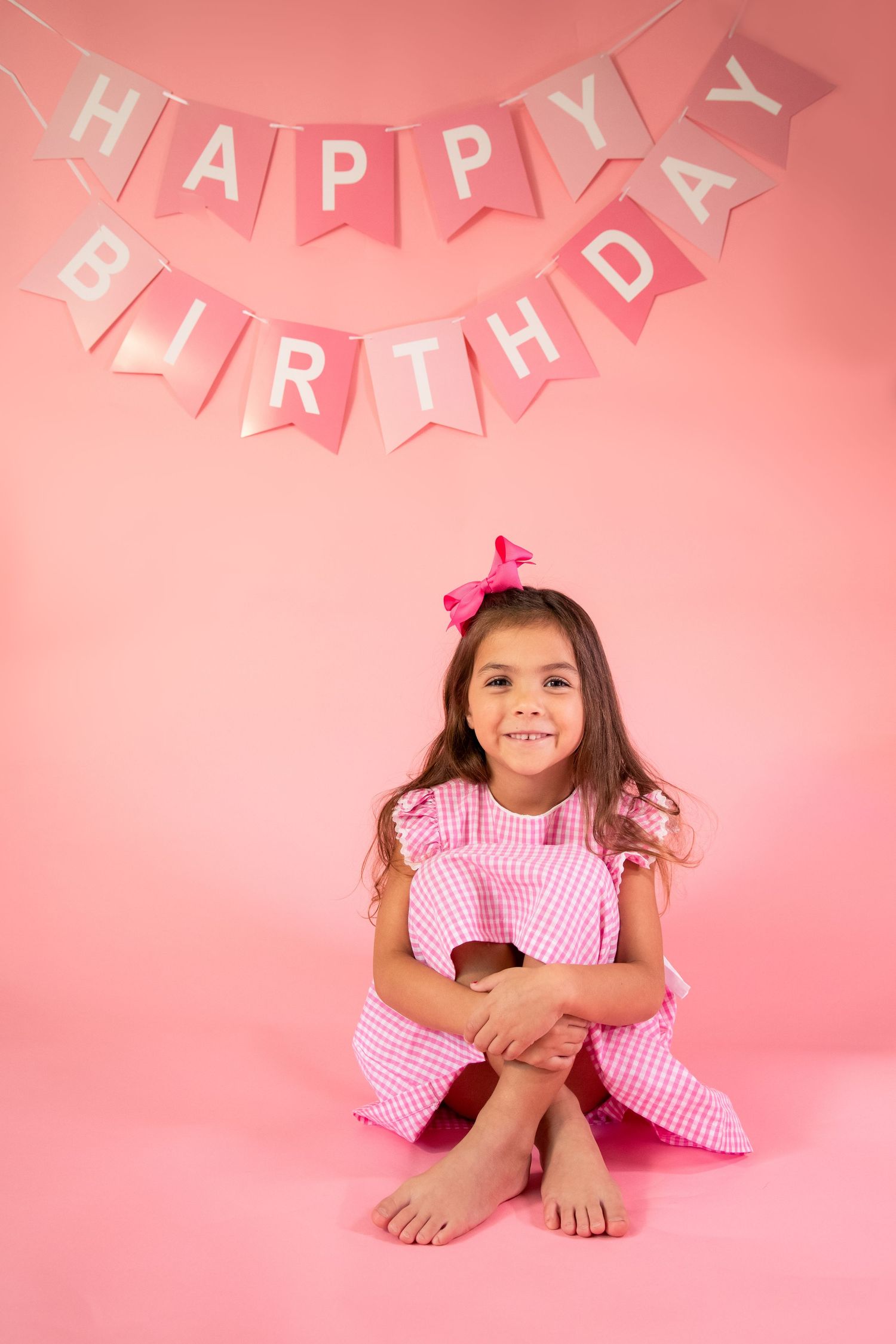 Pink and white gingham dress photographed against coral background with birthday party banner decoration.