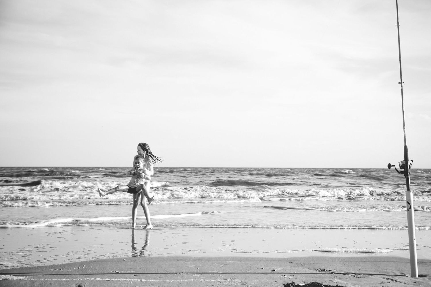 Five connected black and white beach photographs showing someone walking along the shoreline near the ocean waves.