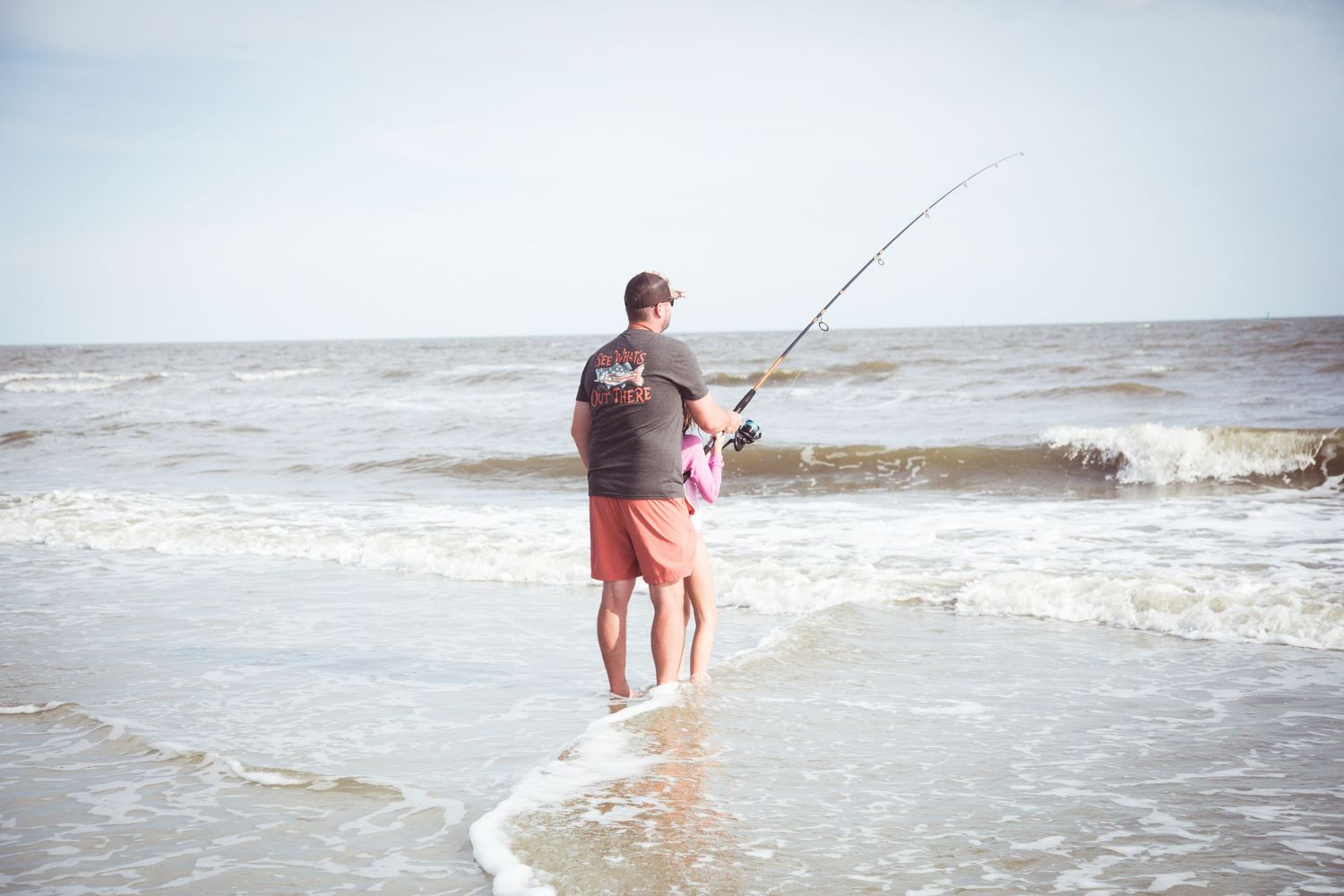 Person surf fishing in the waves on a sunny beach day.