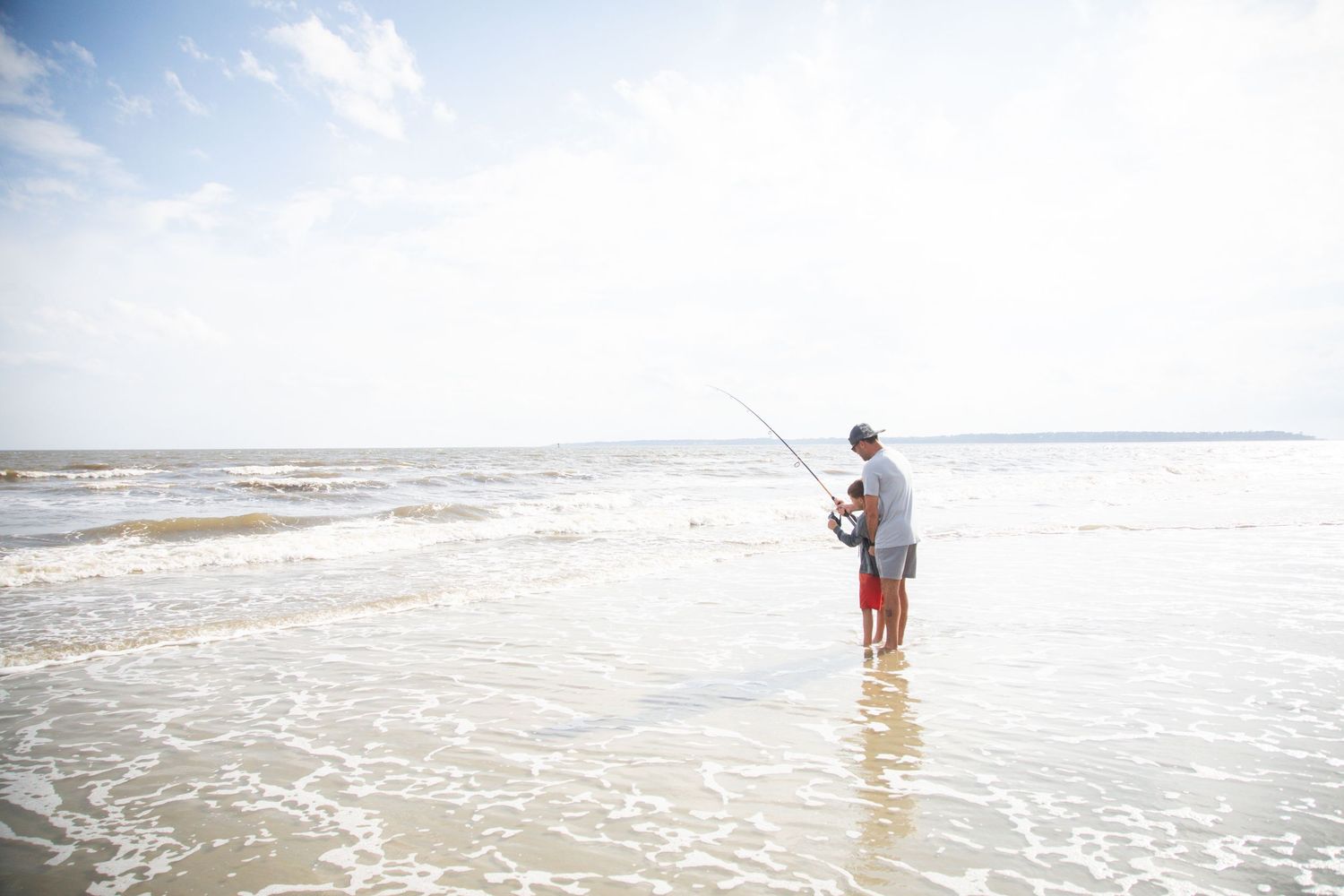 People surf fishing in shallow ocean waters during a bright sunny day.