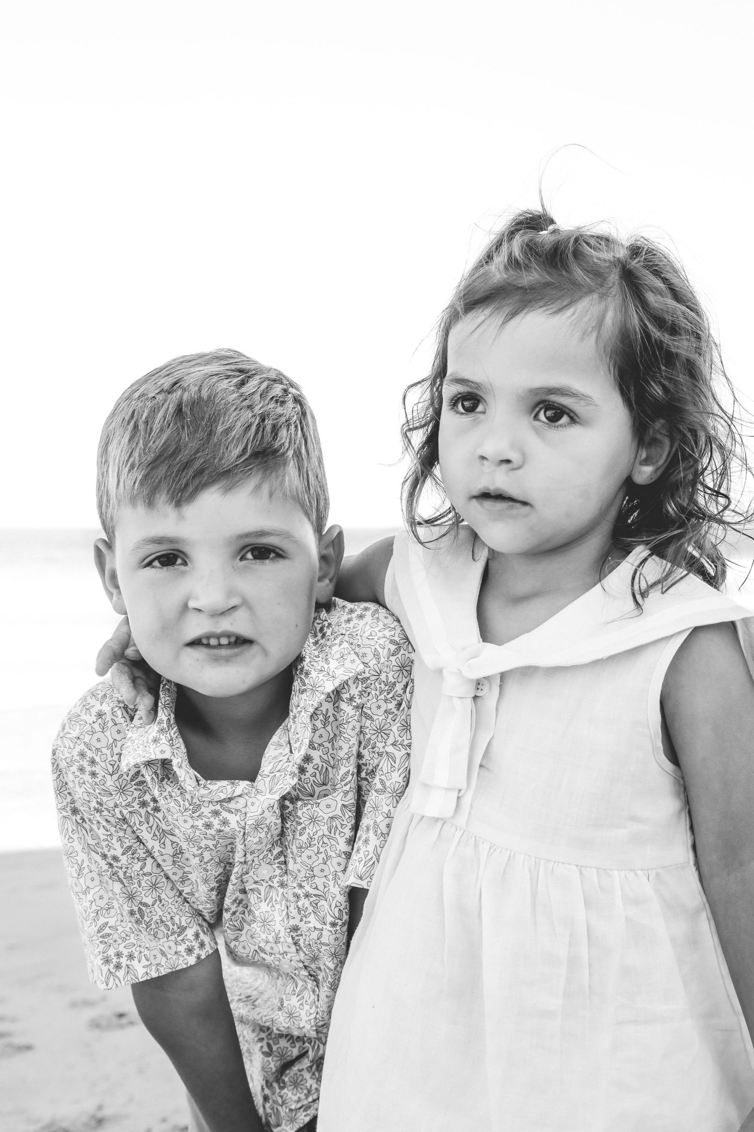 A black and white portrait of two young children standing together outdoors.