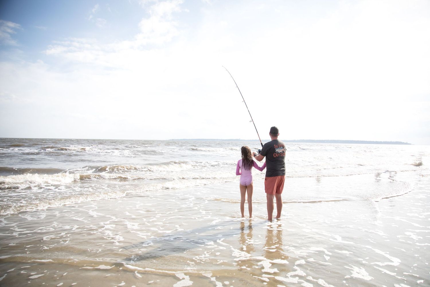 Two people walking along the shoreline at sunset as gentle waves roll onto a sandy beach.