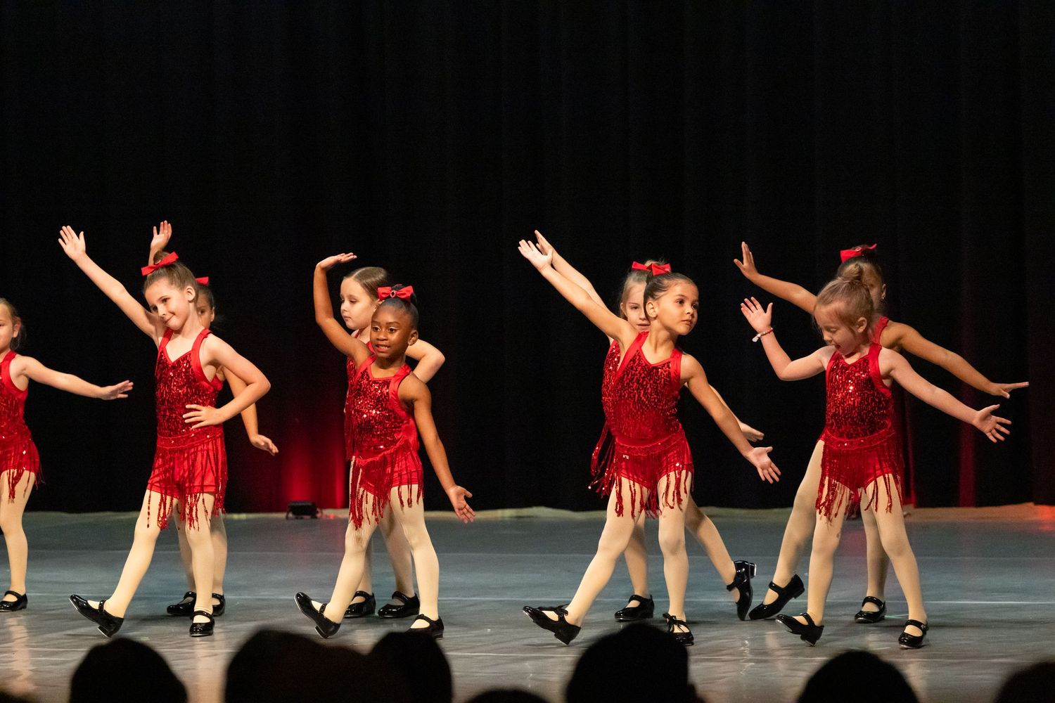 Young dancers in red sparkly costumes perform a synchronized routine on stage during a dance recital.