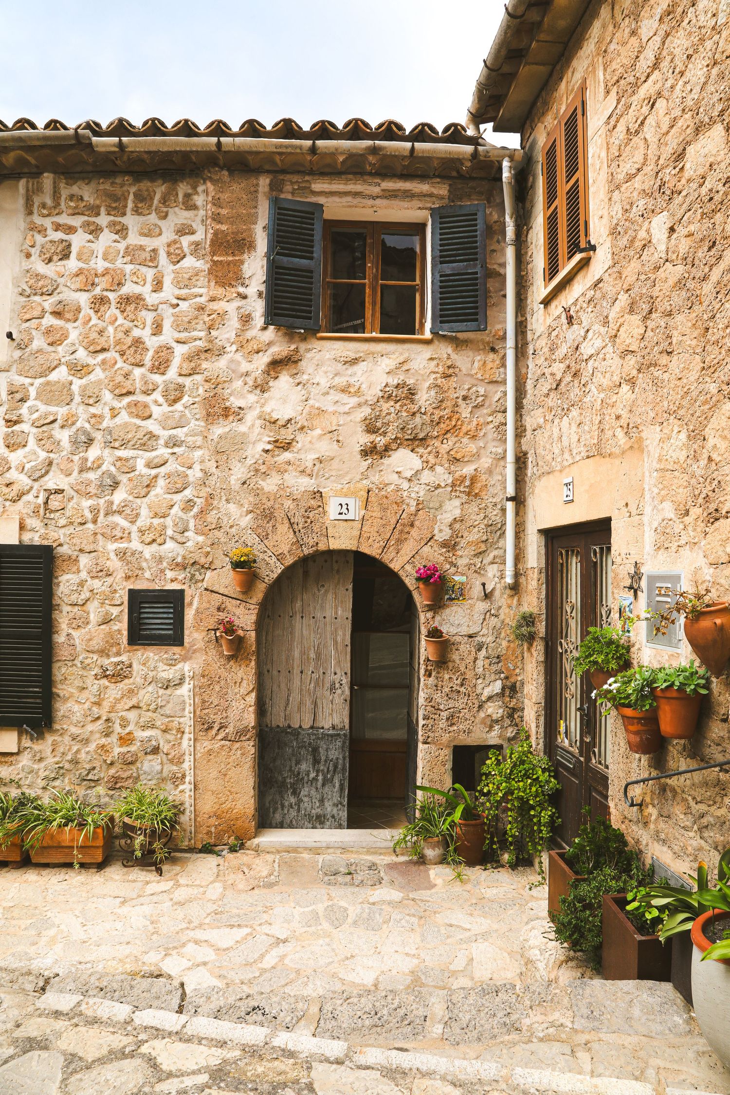 Rustic stone house facade with wooden door, green shutters and potted plants in a charming Mediterranean village.