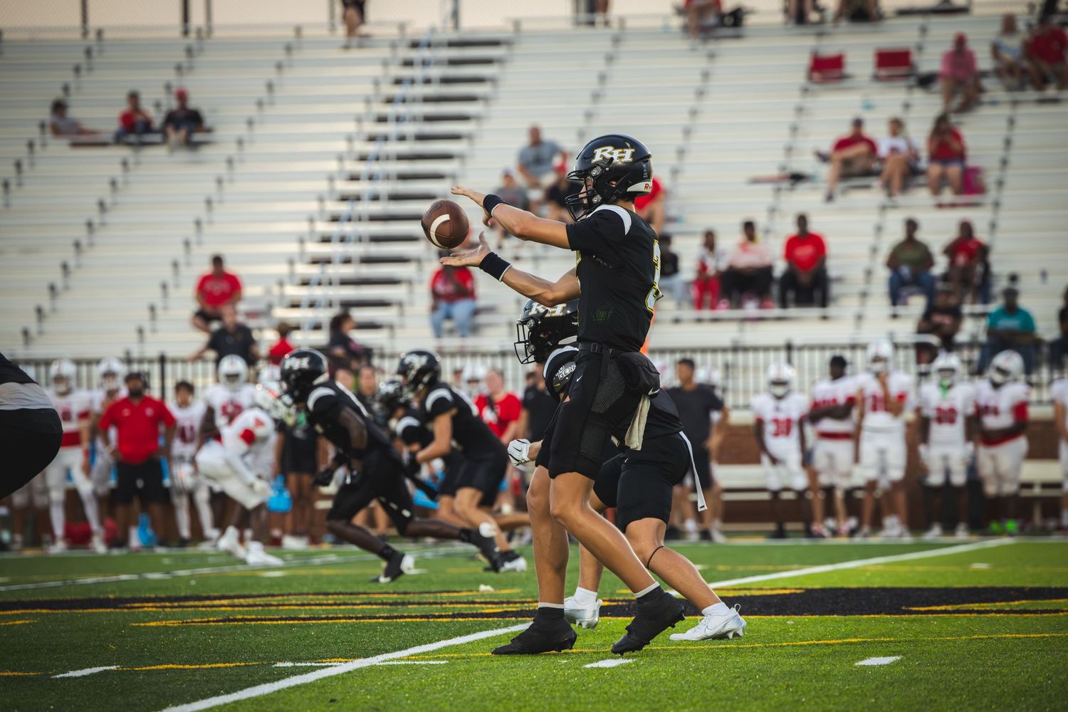 Football player in black uniform catches ball during game with sparse crowd in stadium bleachers.