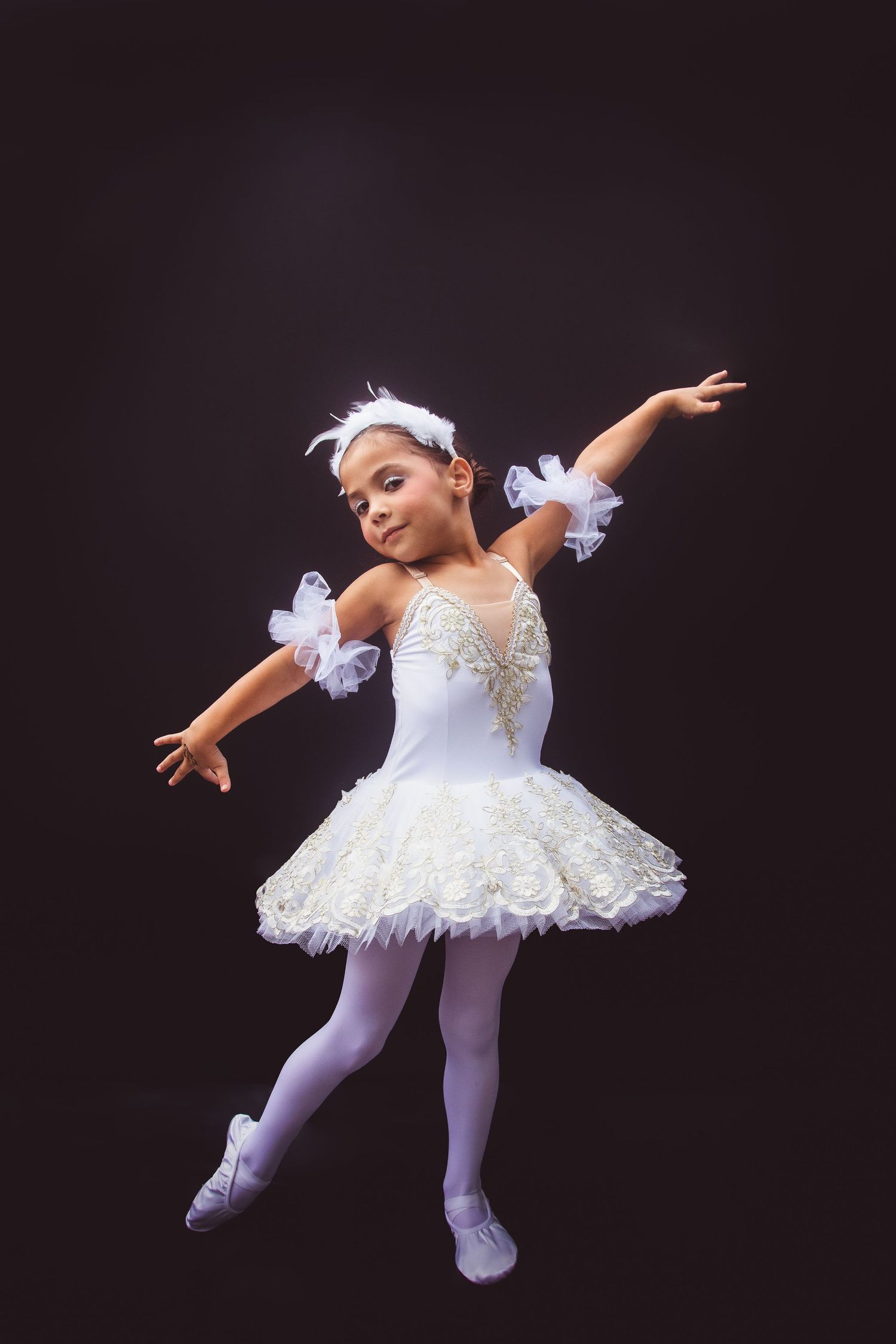 A ballet dancer in a white tutu and tights performs graceful poses against a black background in a four-part series.