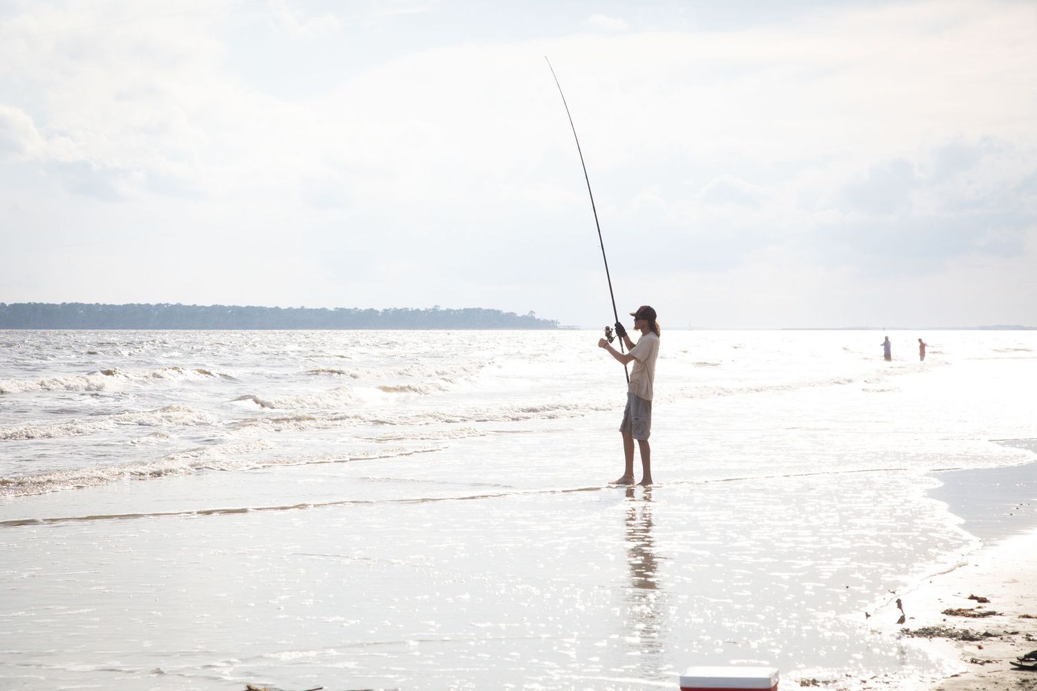 People surf fishing at the beach on a bright sunny day with waves rolling in.