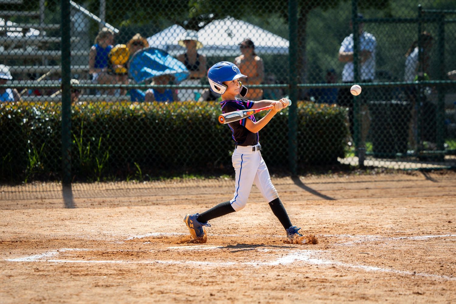 Young boy in baseball uniform swinging bat at pitch during little league game on sunny day.