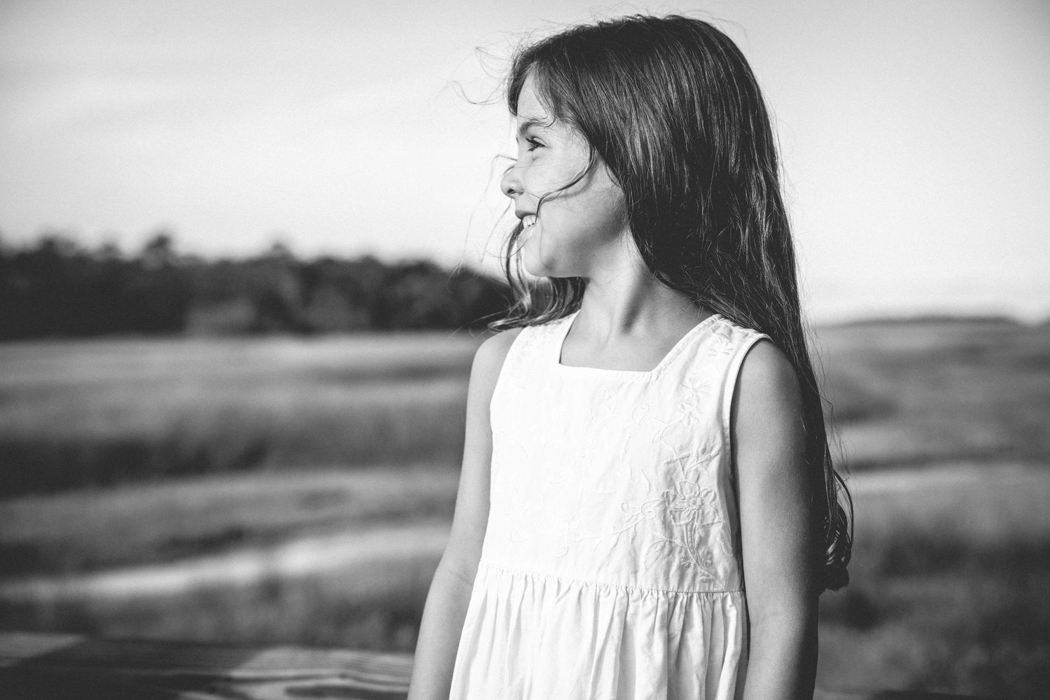 Black and white portrait of a child in a white dress looking to the side against a scenic backdrop.