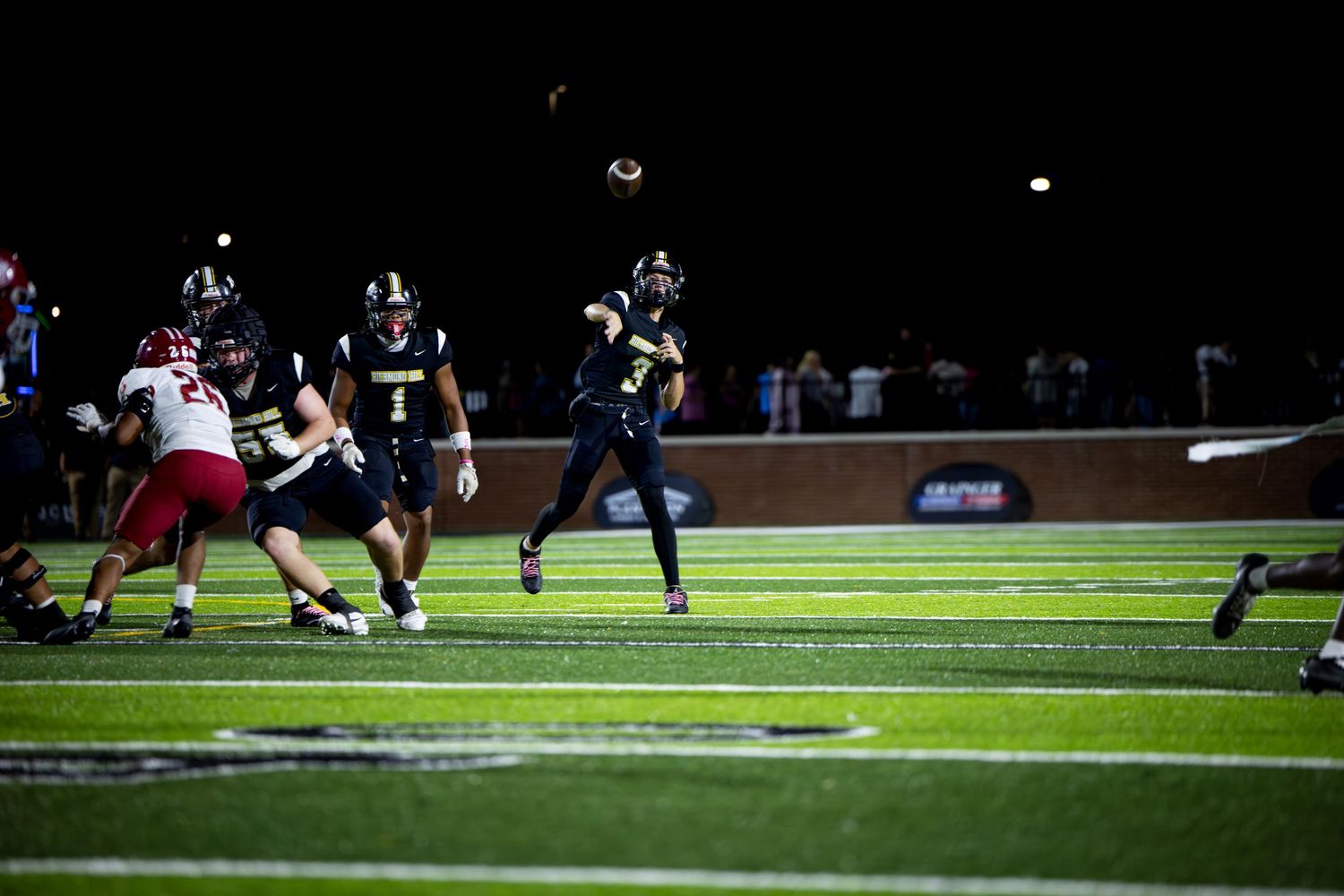 Football players compete during a night game under bright stadium lights as they battle for field position.