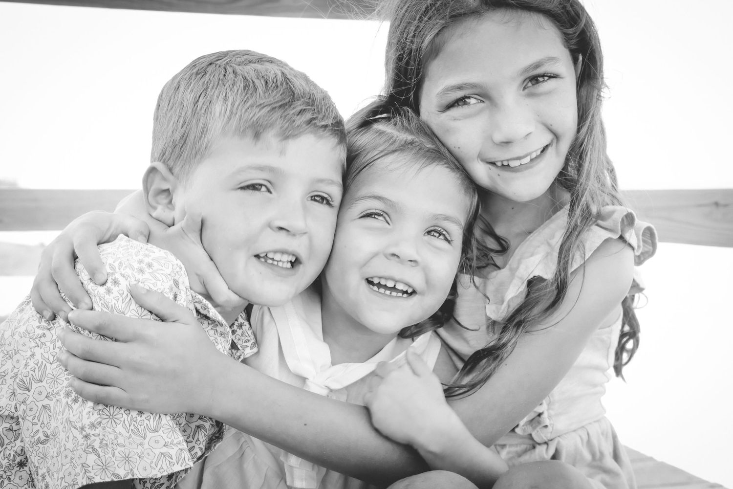 Black and white photo of three children hugging and laughing together outdoors.