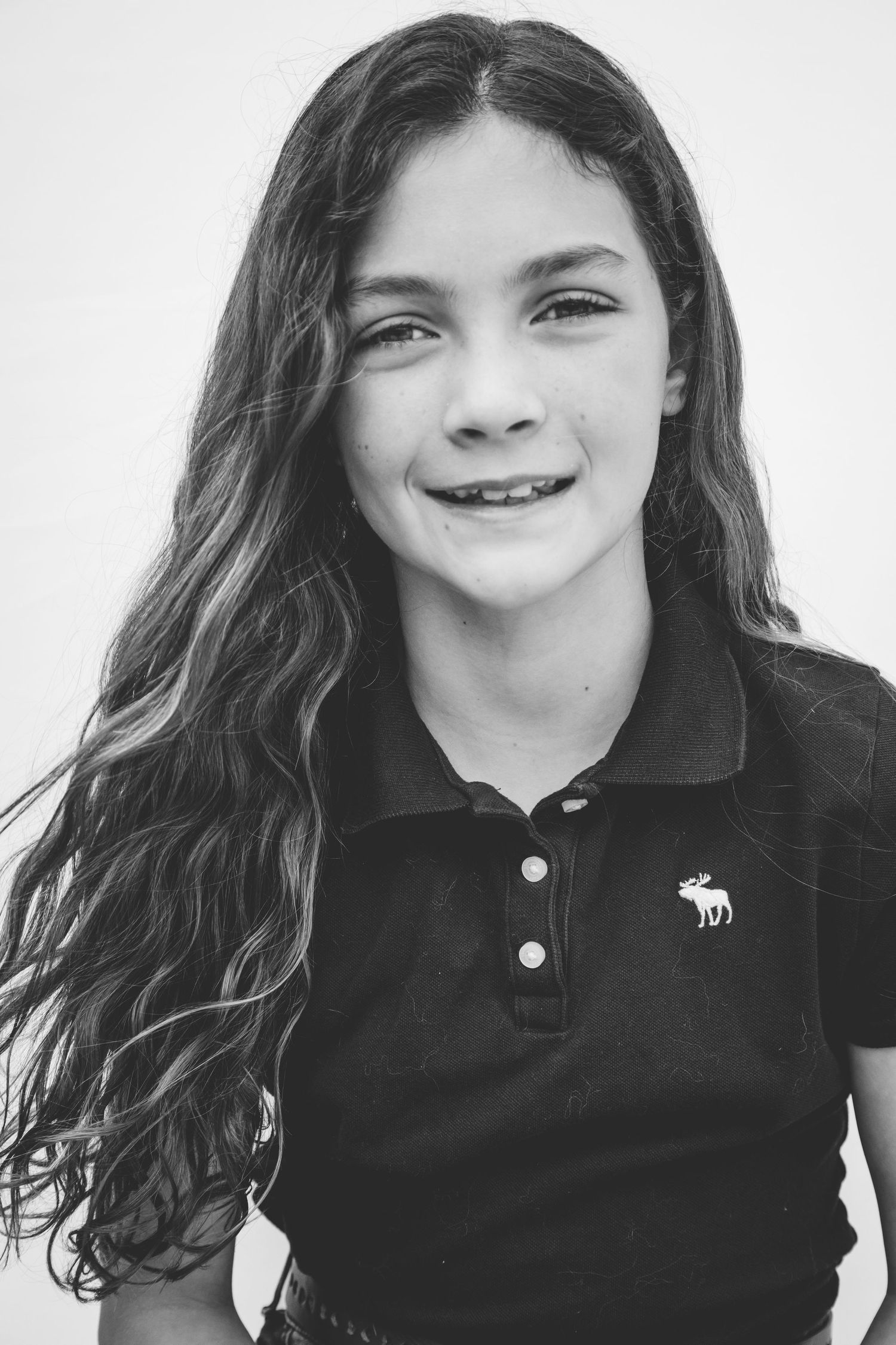 A black and white portrait photo showing someone with long dark hair wearing a collared polo shirt with a logo.