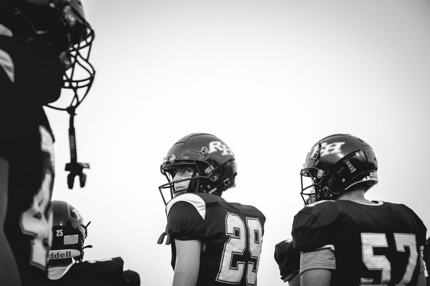 Black and white silhouettes of football players in helmets and uniforms lined up on the field during practice.