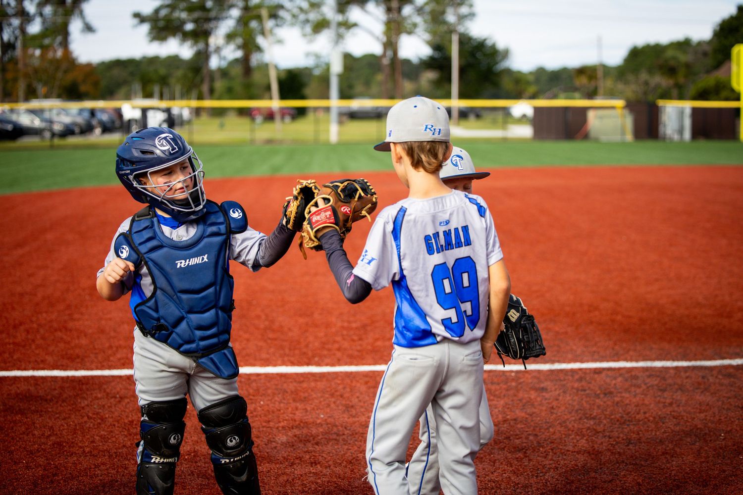 A baseball catcher and pitcher interact on a red clay baseball field during a youth game.
