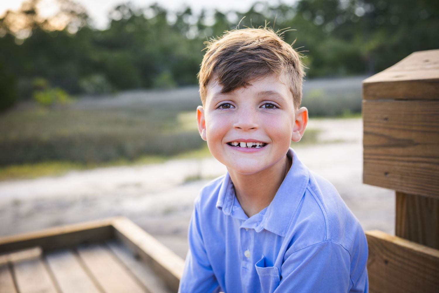 Child wearing blue collared shirt photographed close up on wooden deck with natural lighting.