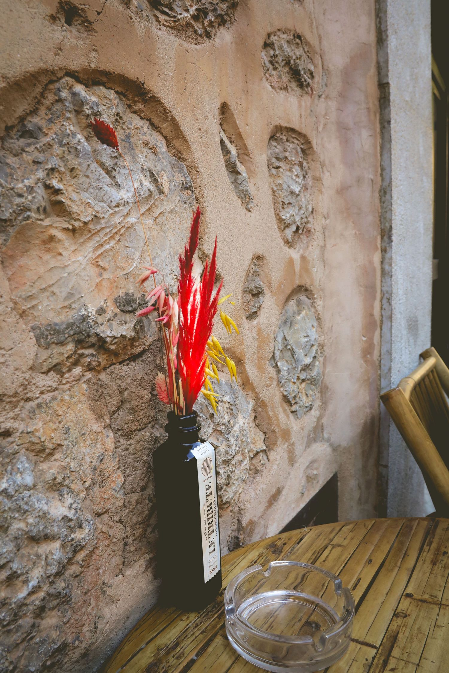 Several plastic red feather dusters stand propped against a rustic stone wall on a wooden shelf.