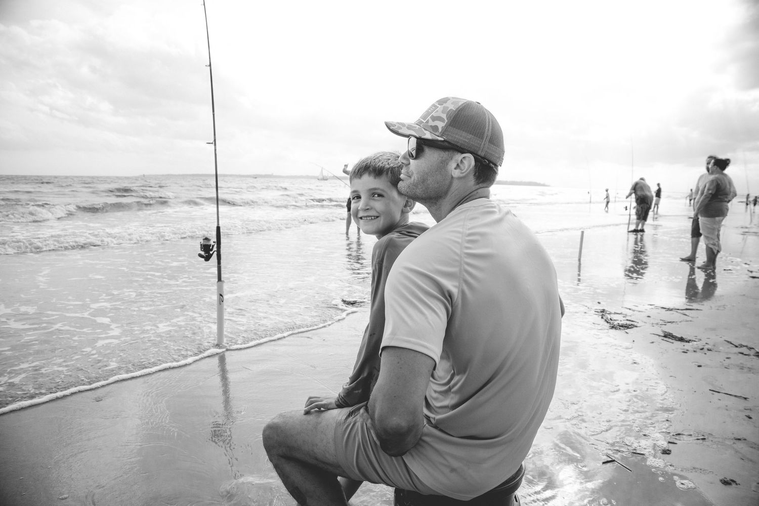 A serene beach scene showing fishing activity along the shoreline as waves roll in on an overcast day.