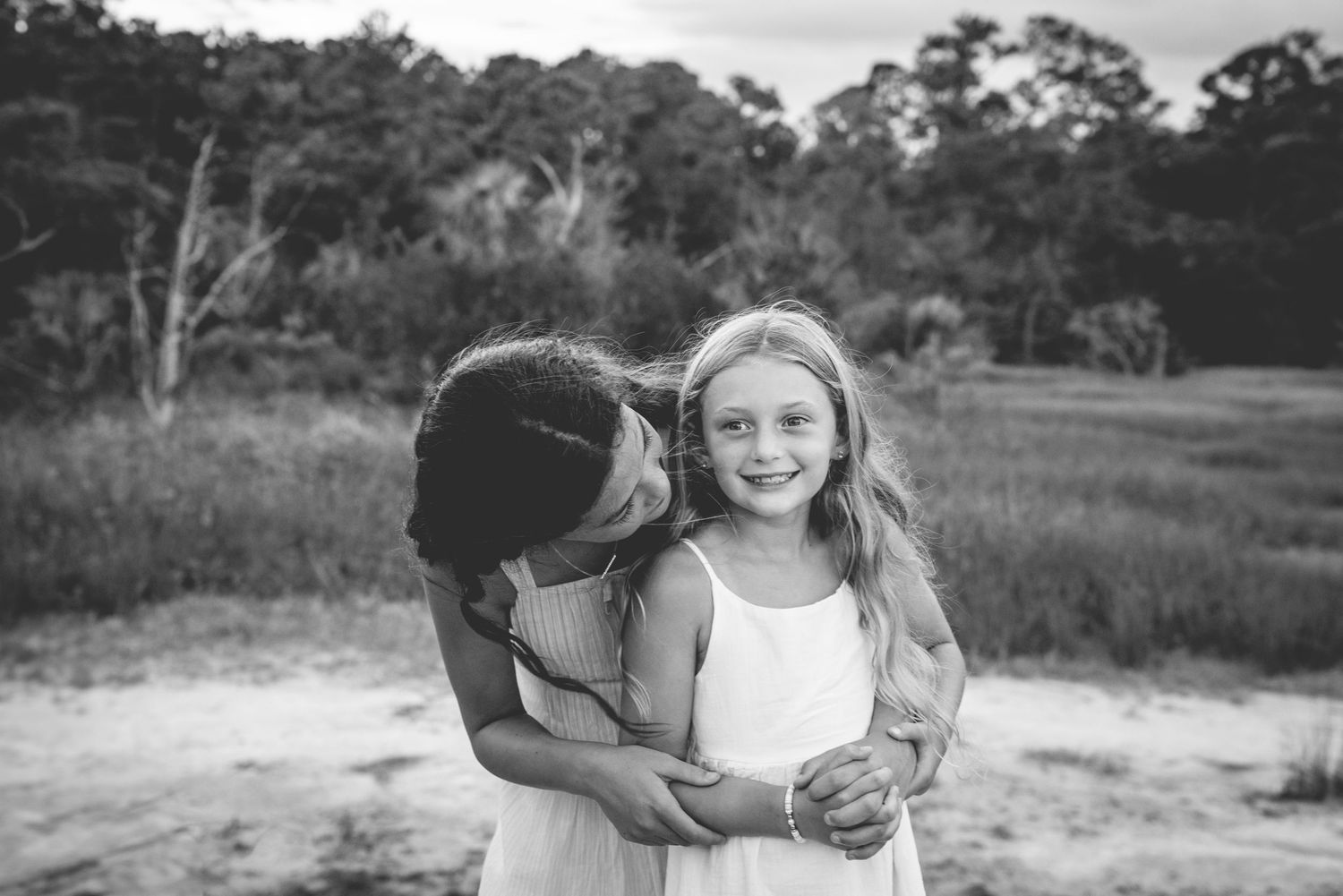 Two young friends share a tender moment together outdoors in a black and white photograph.
