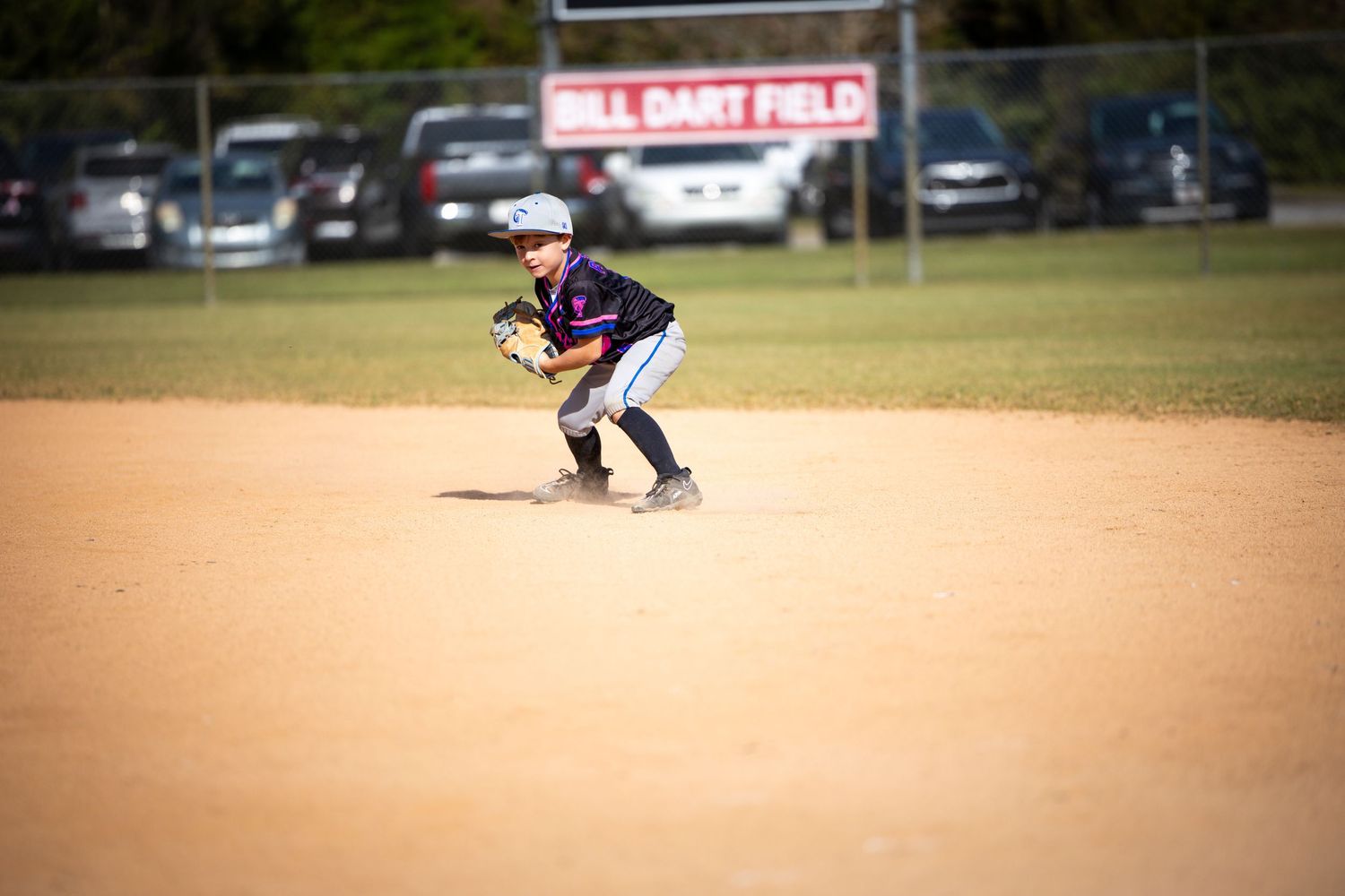 Baseball player in blue uniform swings bat during game on dirt infield at local baseball field.
