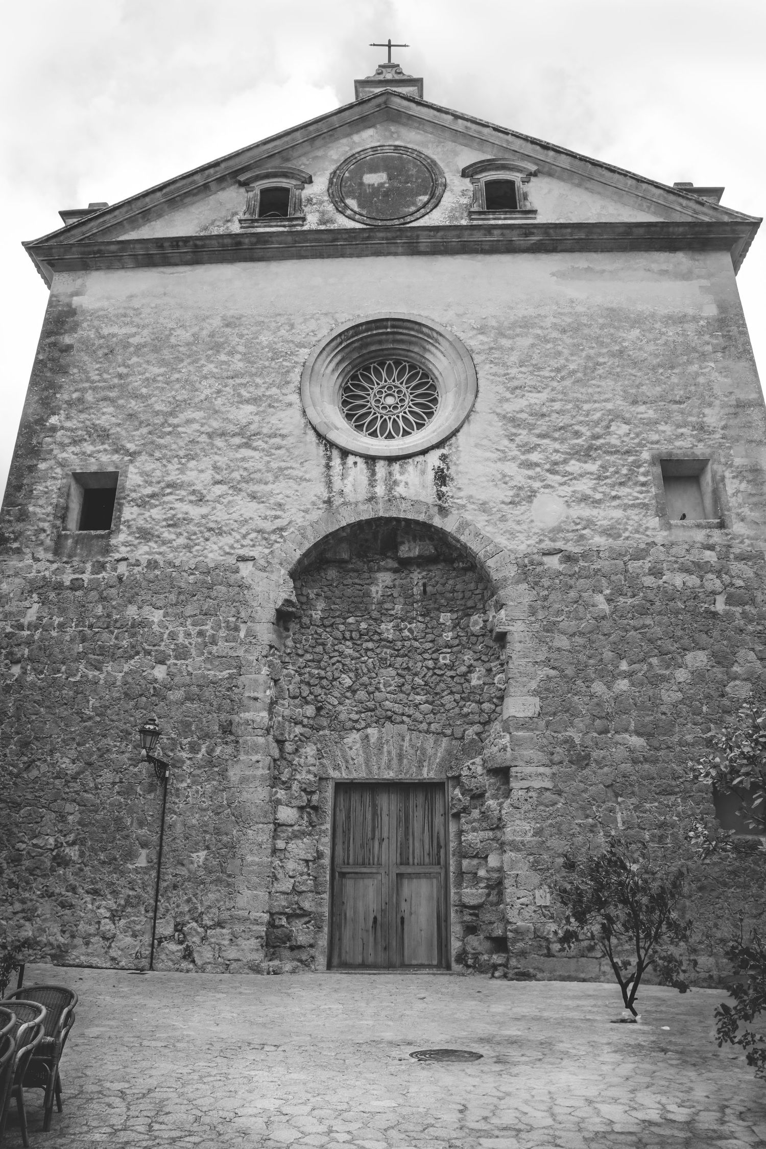Stone facade of three historic church buildings with rustic wooden doors and circular rose windows in a courtyard.