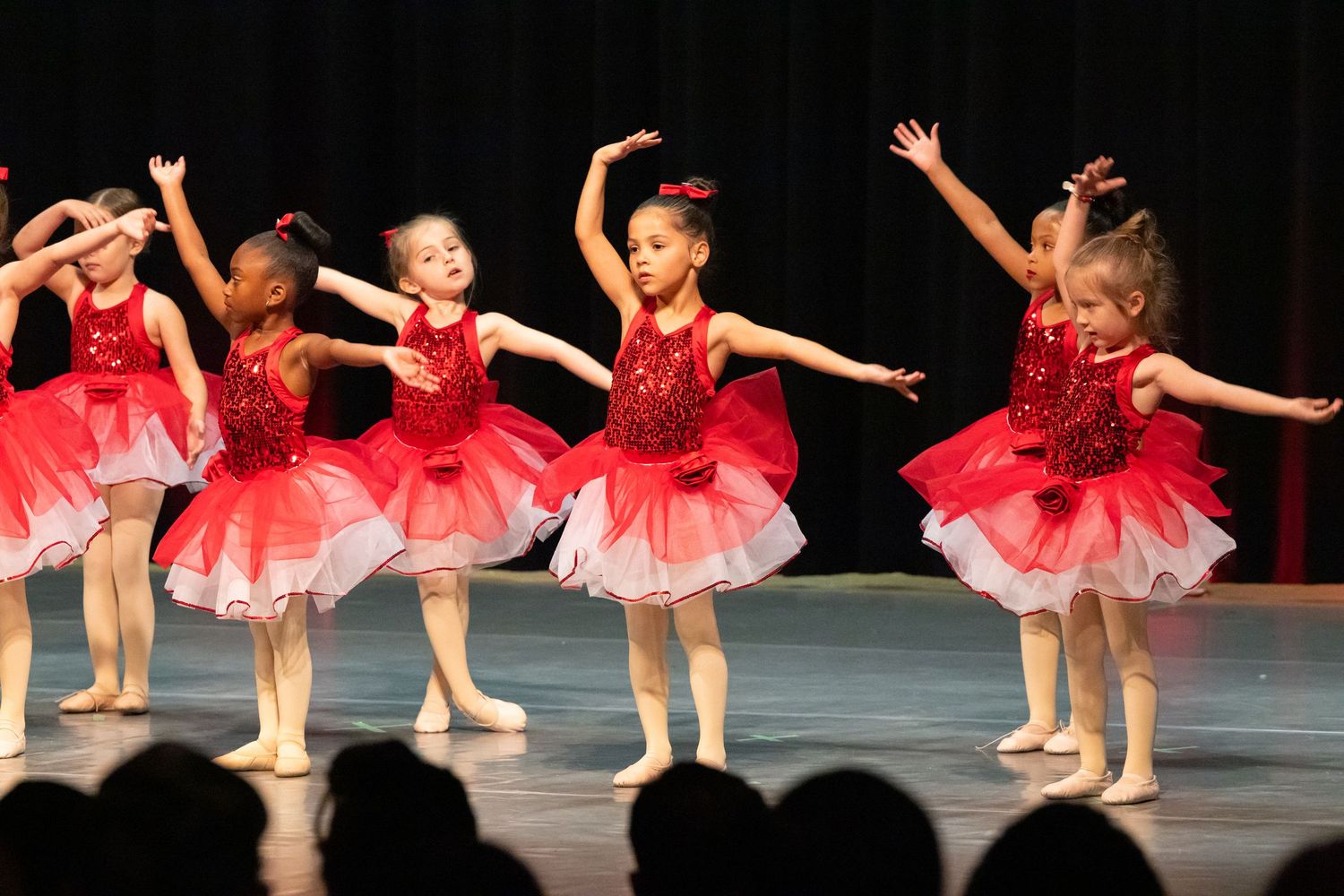 Young ballet dancers in pink tutus perform on stage during a dance recital with theatrical lighting.