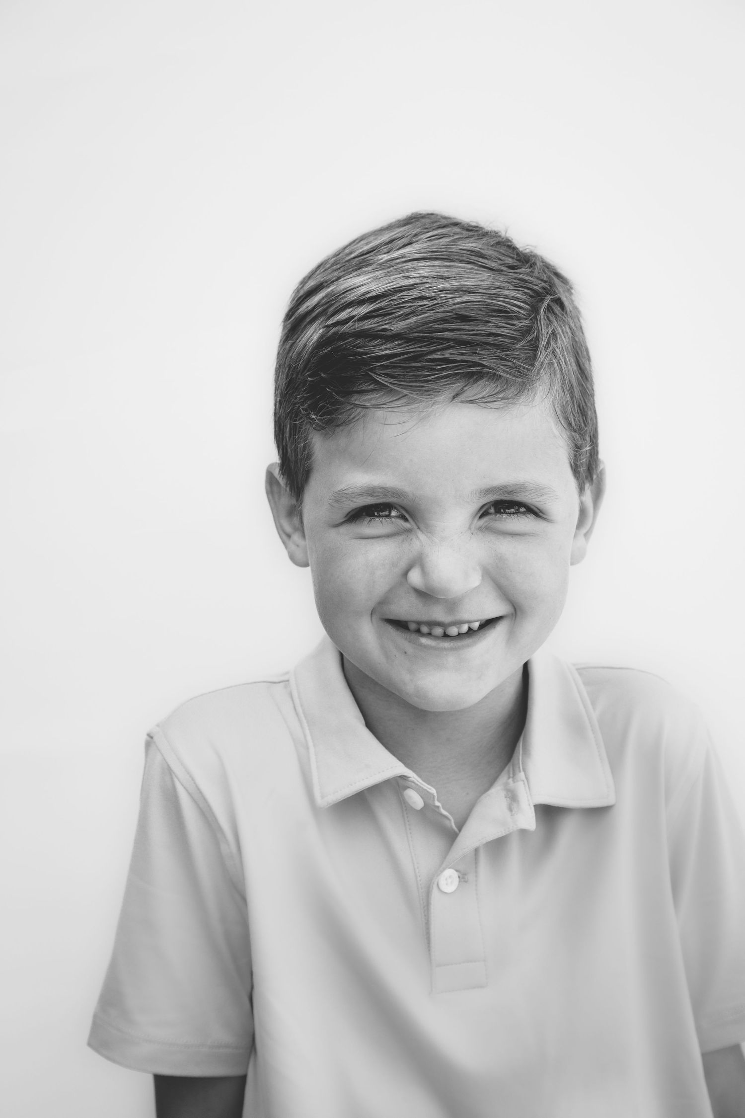 Black and white portrait of a young child wearing a polo shirt and smiling brightly against a light background.