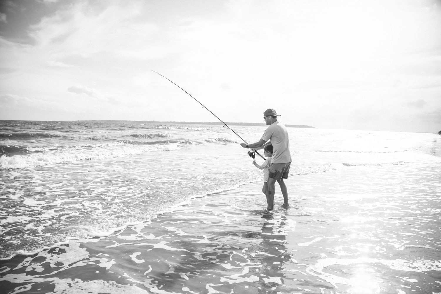 Black and white photo of surf fishing in the ocean waves.