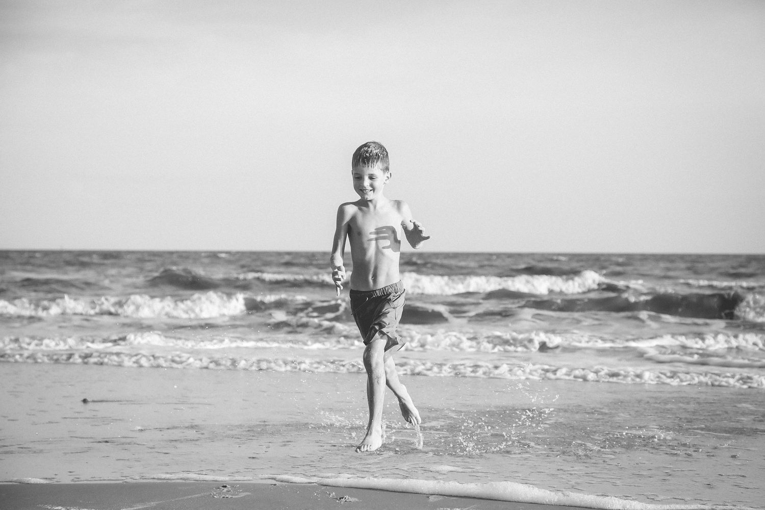 Vintage black and white photograph of someone walking along a beach shore with waves in the background.
