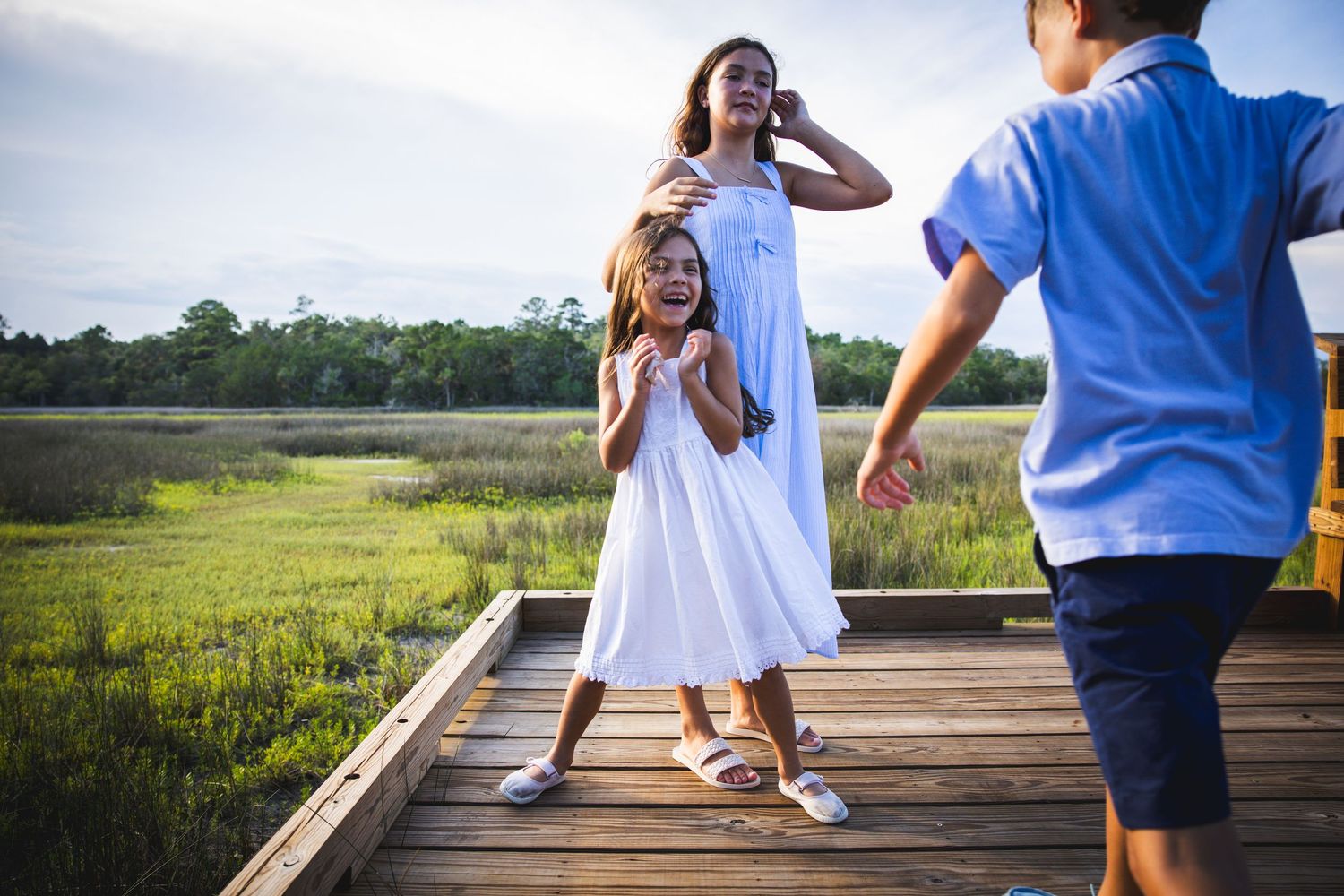 Children playing and laughing together on a wooden boardwalk with marsh views.