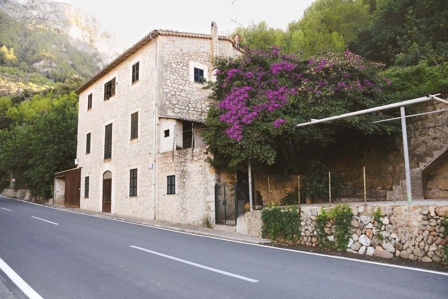 Traditional stone house with purple bougainvillea flowers growing along a mountain road in Mallorca.