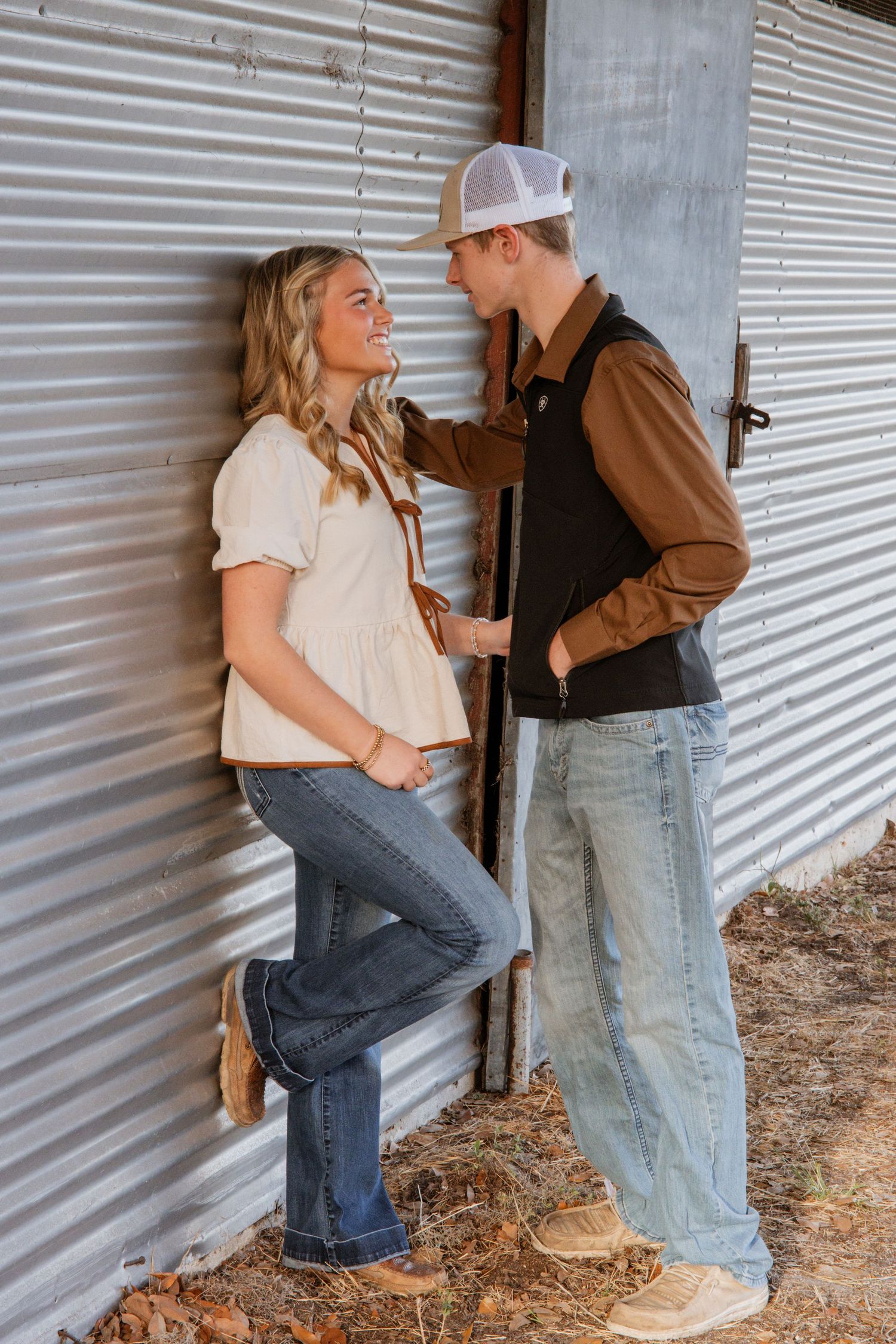 A couple in casual attire shares a tender moment against a corrugated metal wall background.