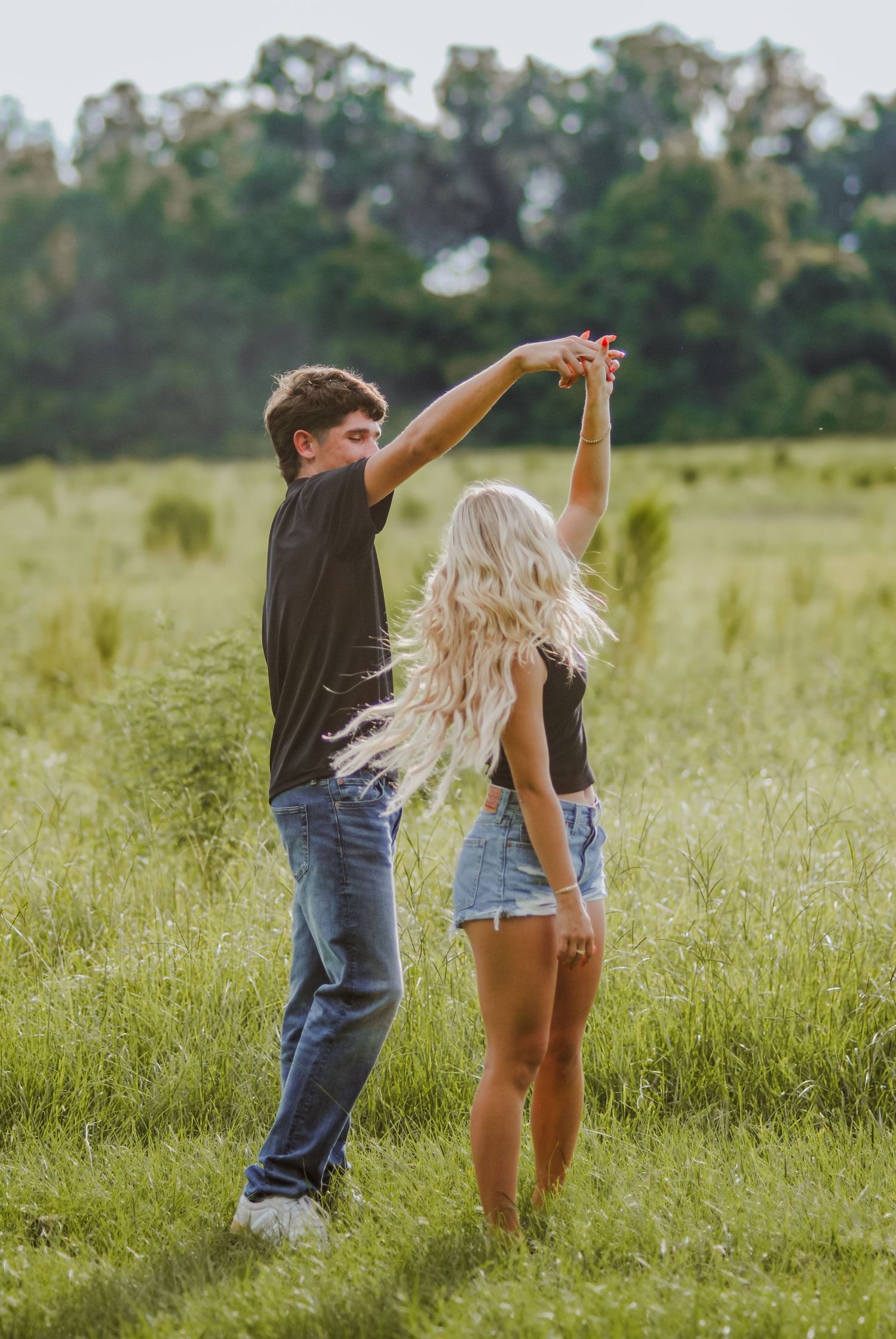 A playful couple dancing together in a sunny meadow with tall grass.