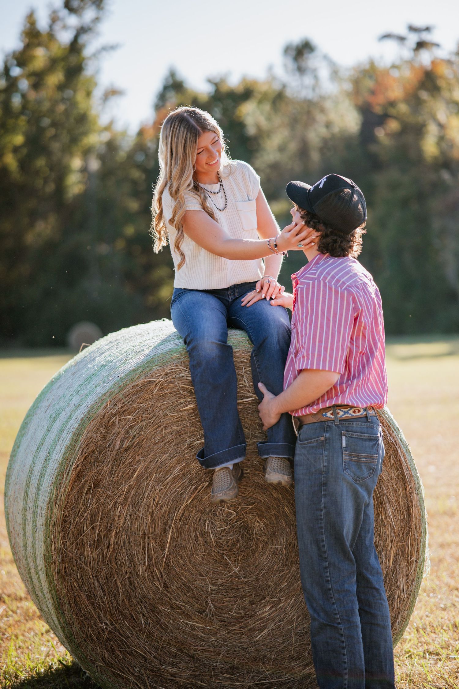 Couple sharing a playful moment on a large hay bale in autumn field.