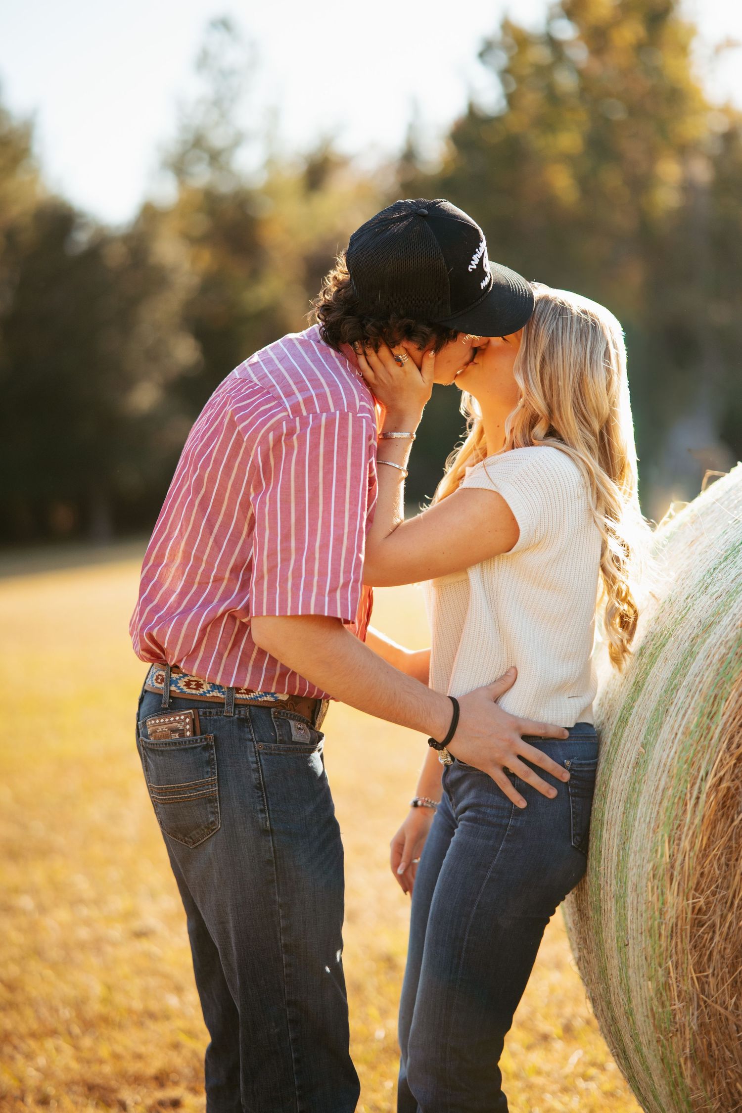 Romantic couple embracing by a hay bale in golden afternoon light.