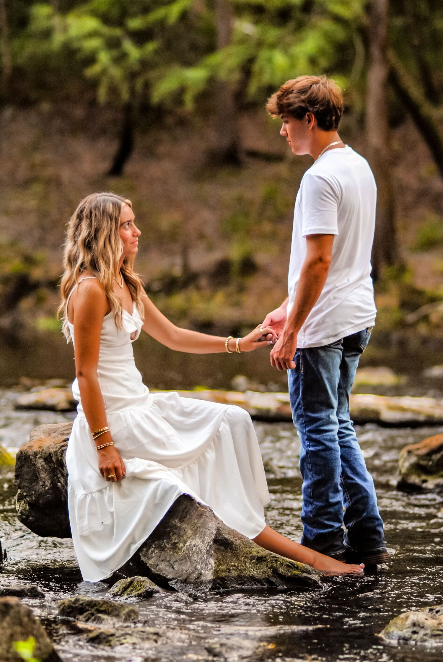 Two people sit together on rocky terrain near flowing water in a natural setting.