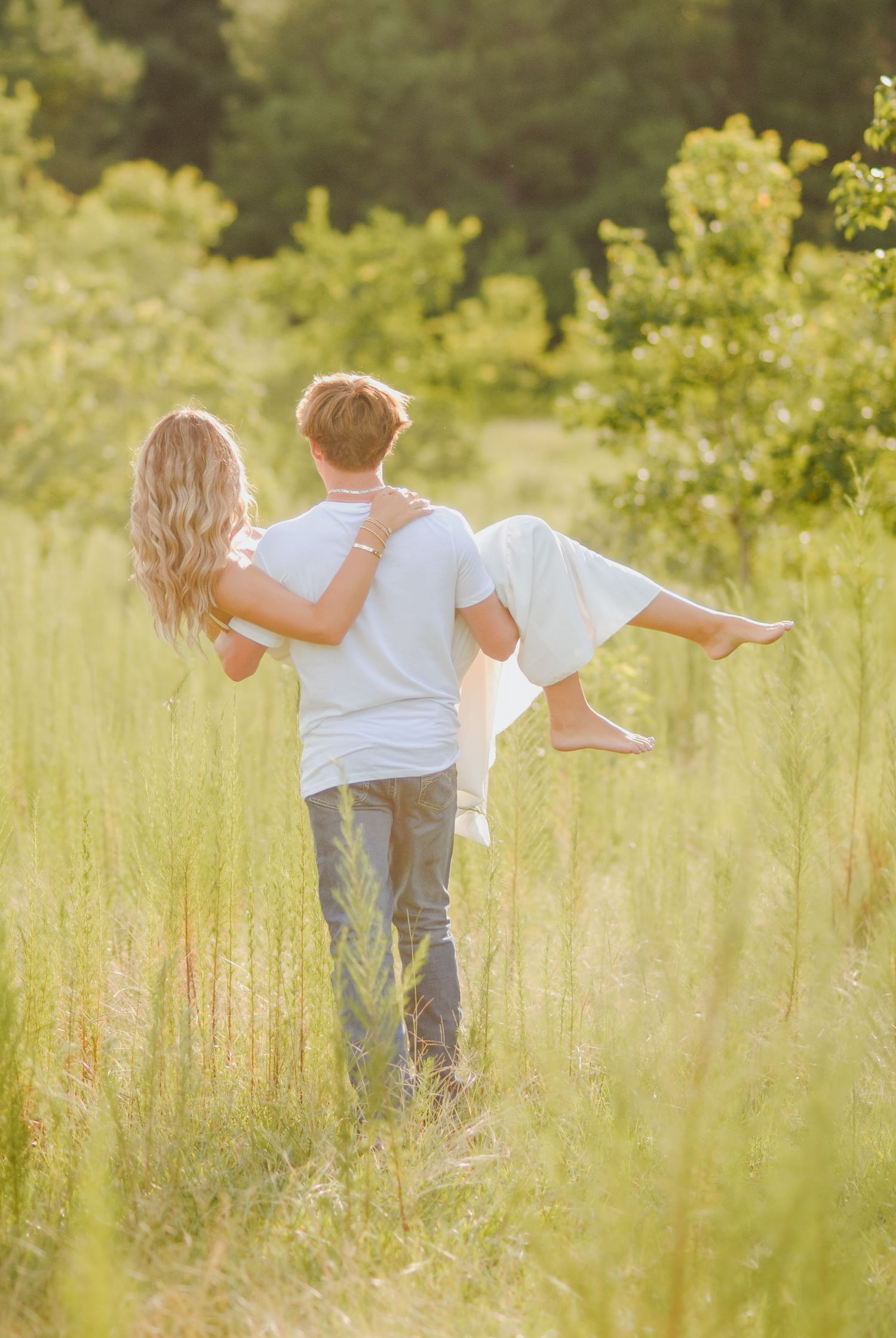 Two people dance and twirl through a sunlit meadow with tall grass swaying around them.