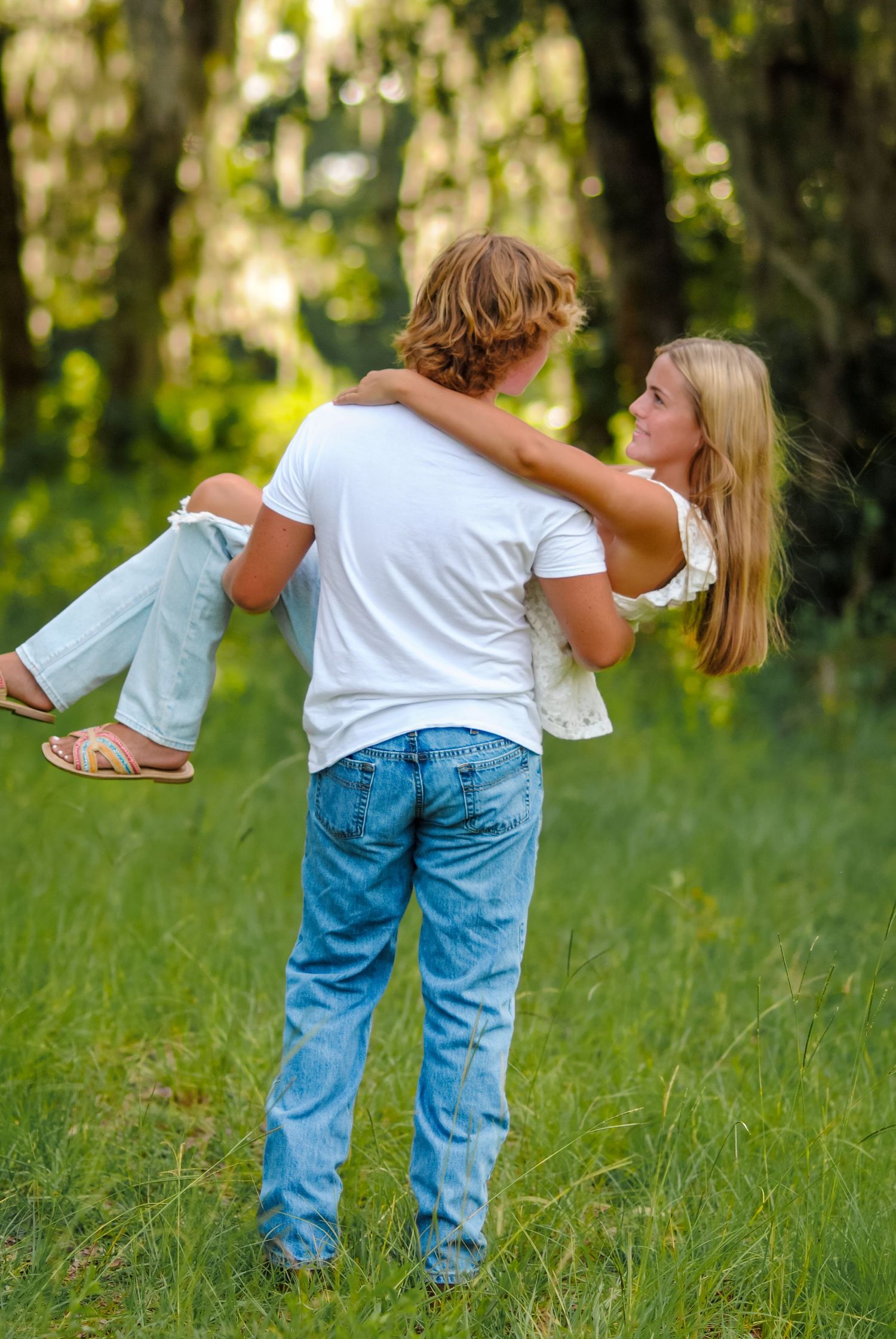 Two people playfully dance in a grassy field with Spanish moss hanging from trees in the background.