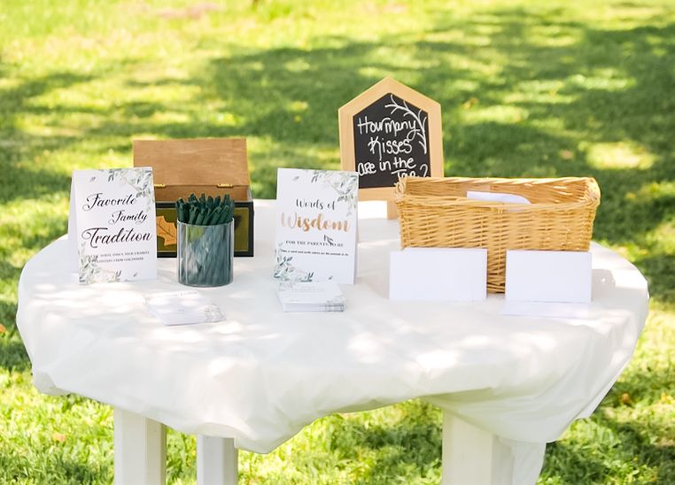 White tables with decorative displays and signs set up outdoors on green grass.