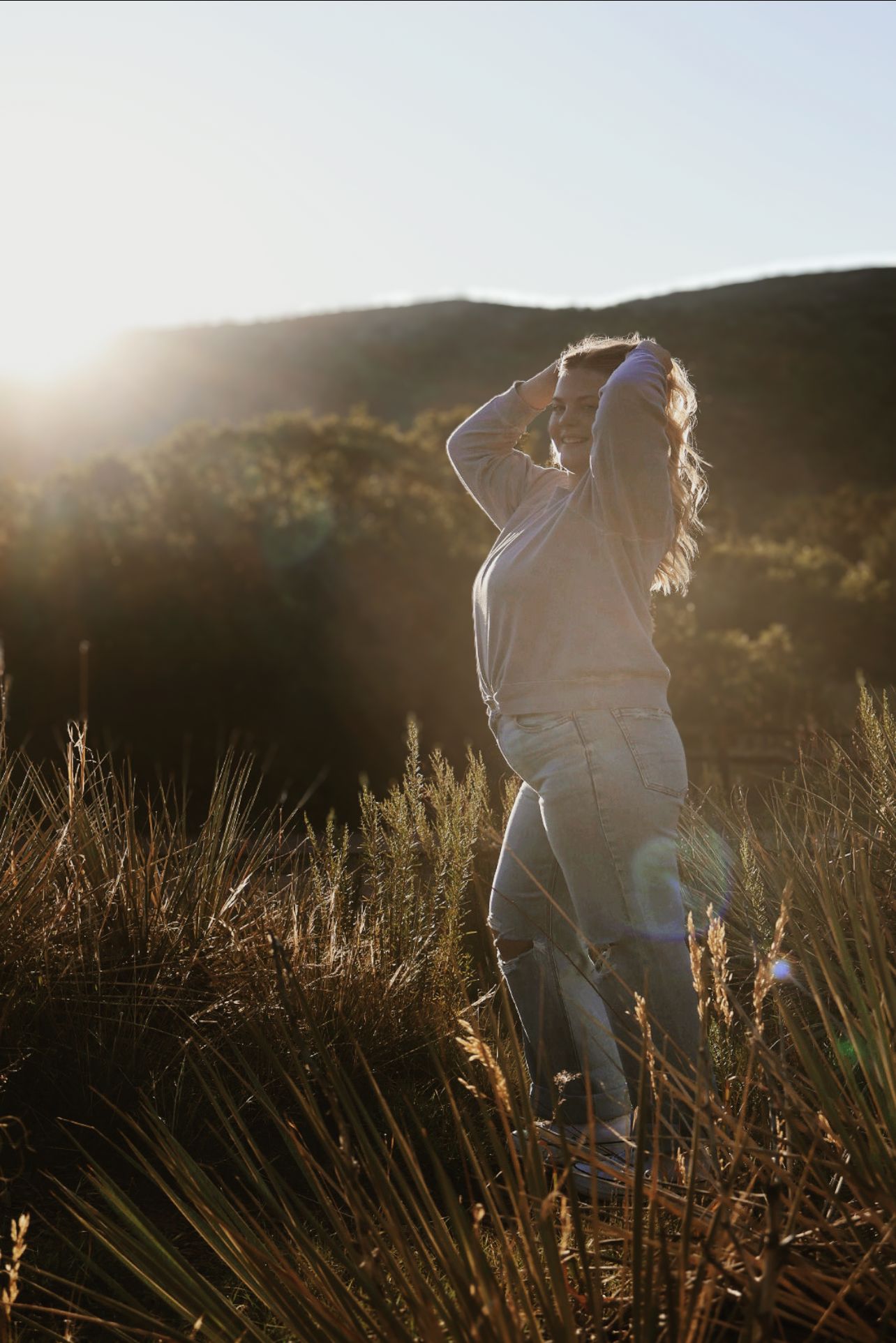 Female senior posing in golden hour sunlight with mountain views during an outdoor senior photography session at Garden of the Gods.
